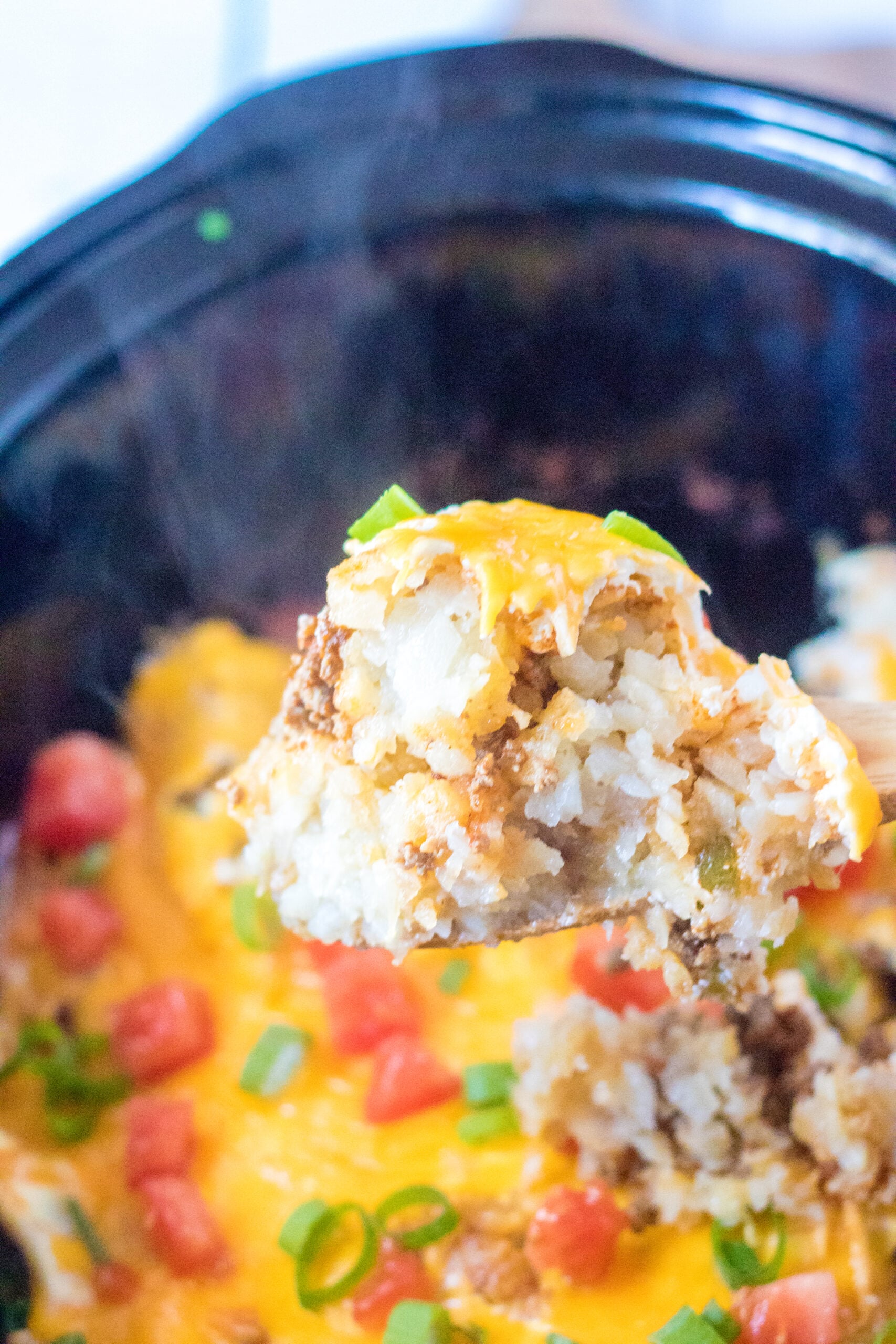 Close up view of a wooden spoon removing a serving of Slow Cooker John Wayne Casserole.