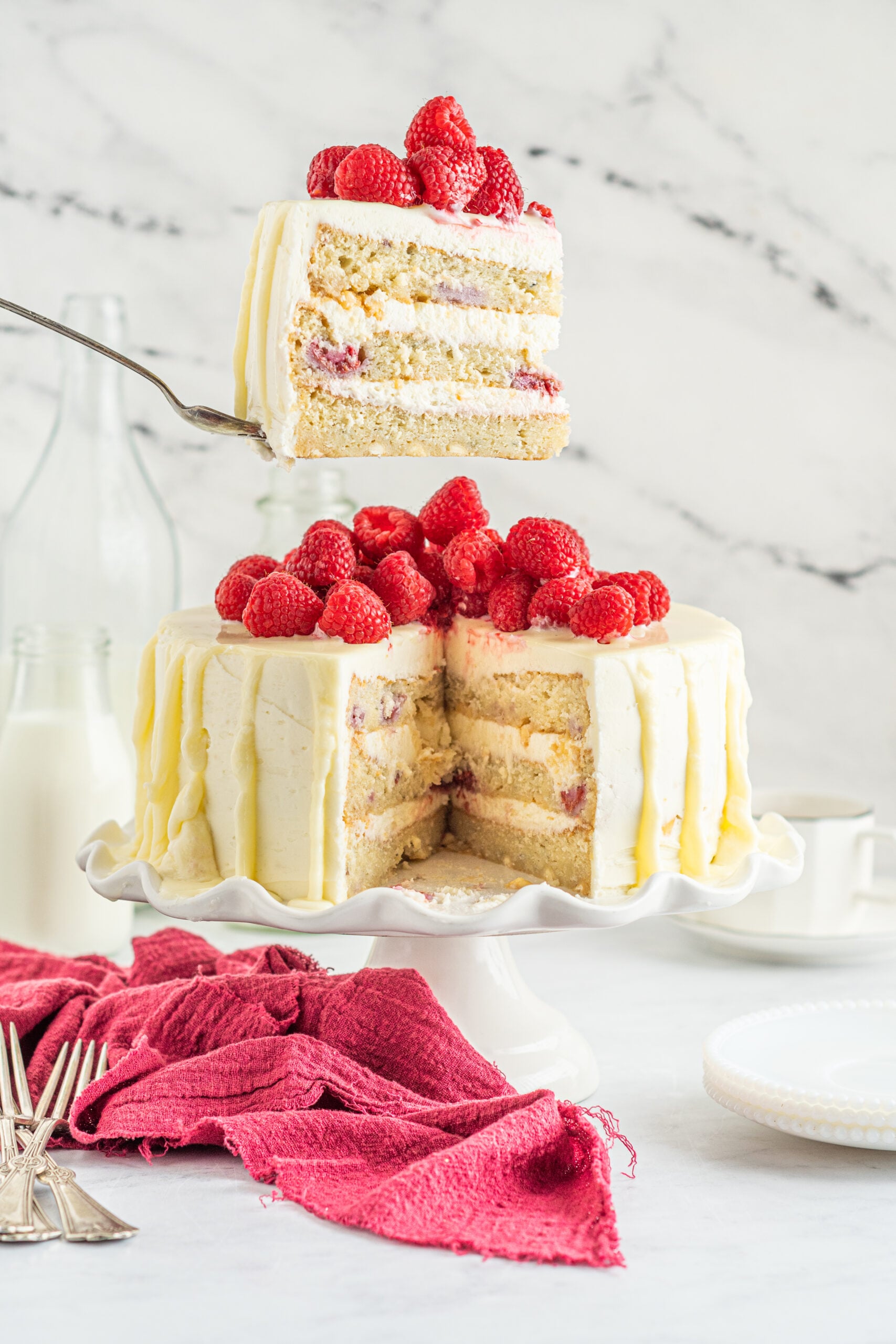 Side view of a slice of White Chocolate Cake with Raspberries on a silver cake server.