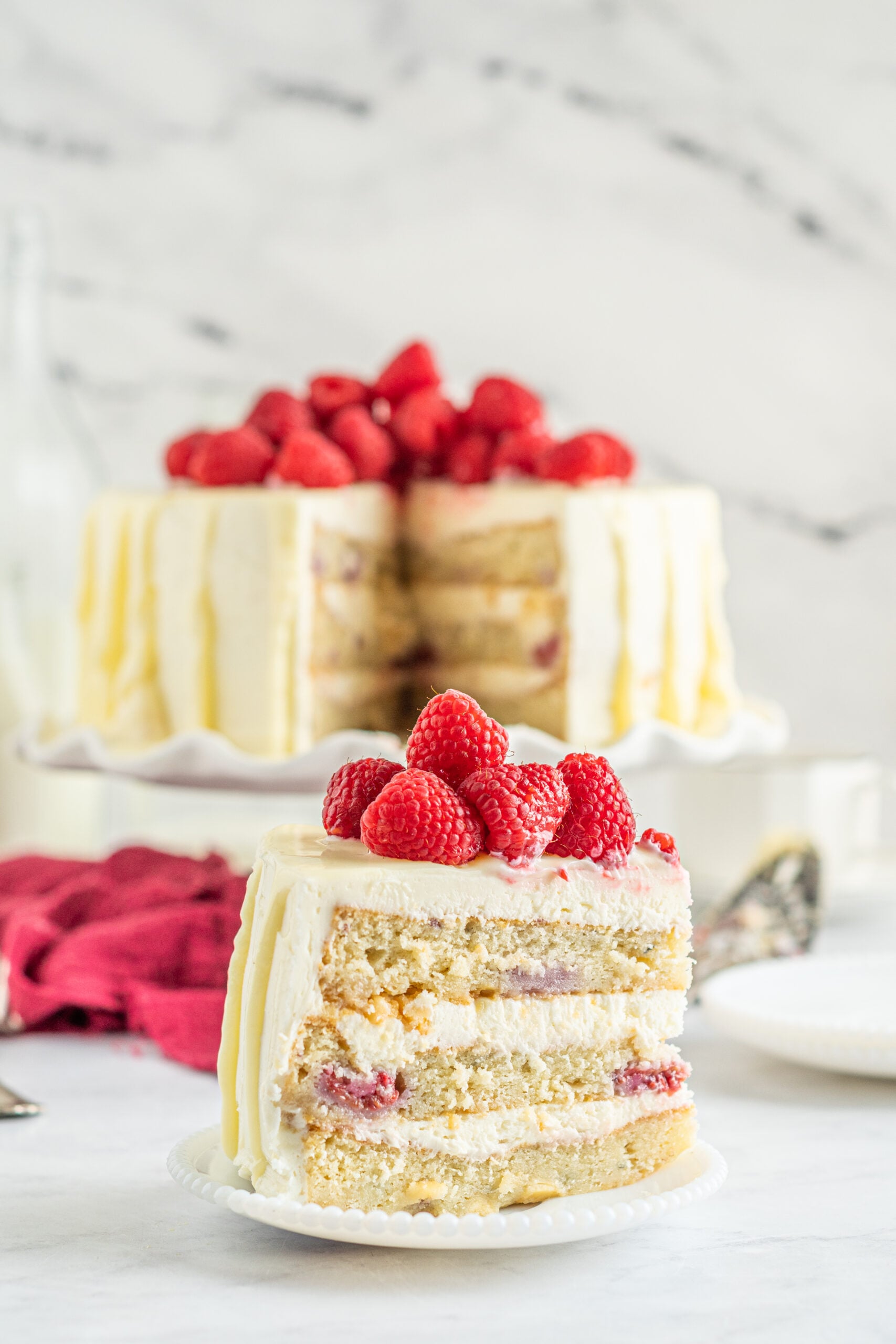 Side view of a slice of White Chocolate Cake with Raspberries on a white plate.