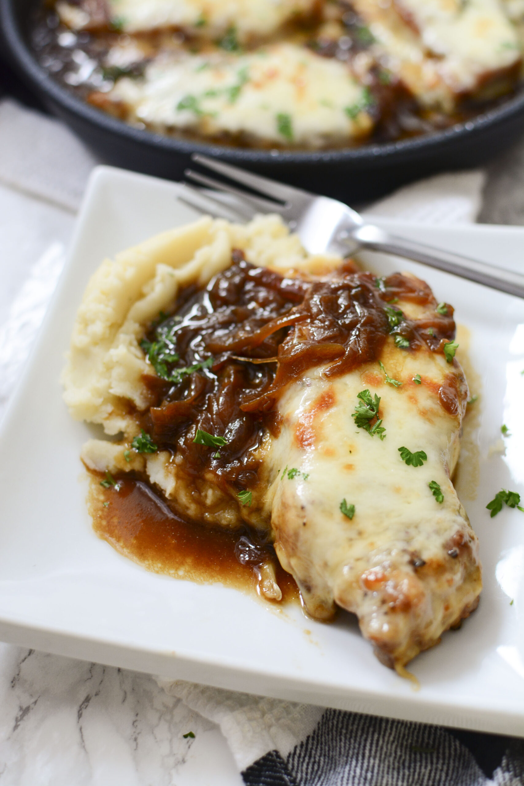 Close up view of French Onion Pork Chops served with mashed potatoes and silver fork on a white plate.