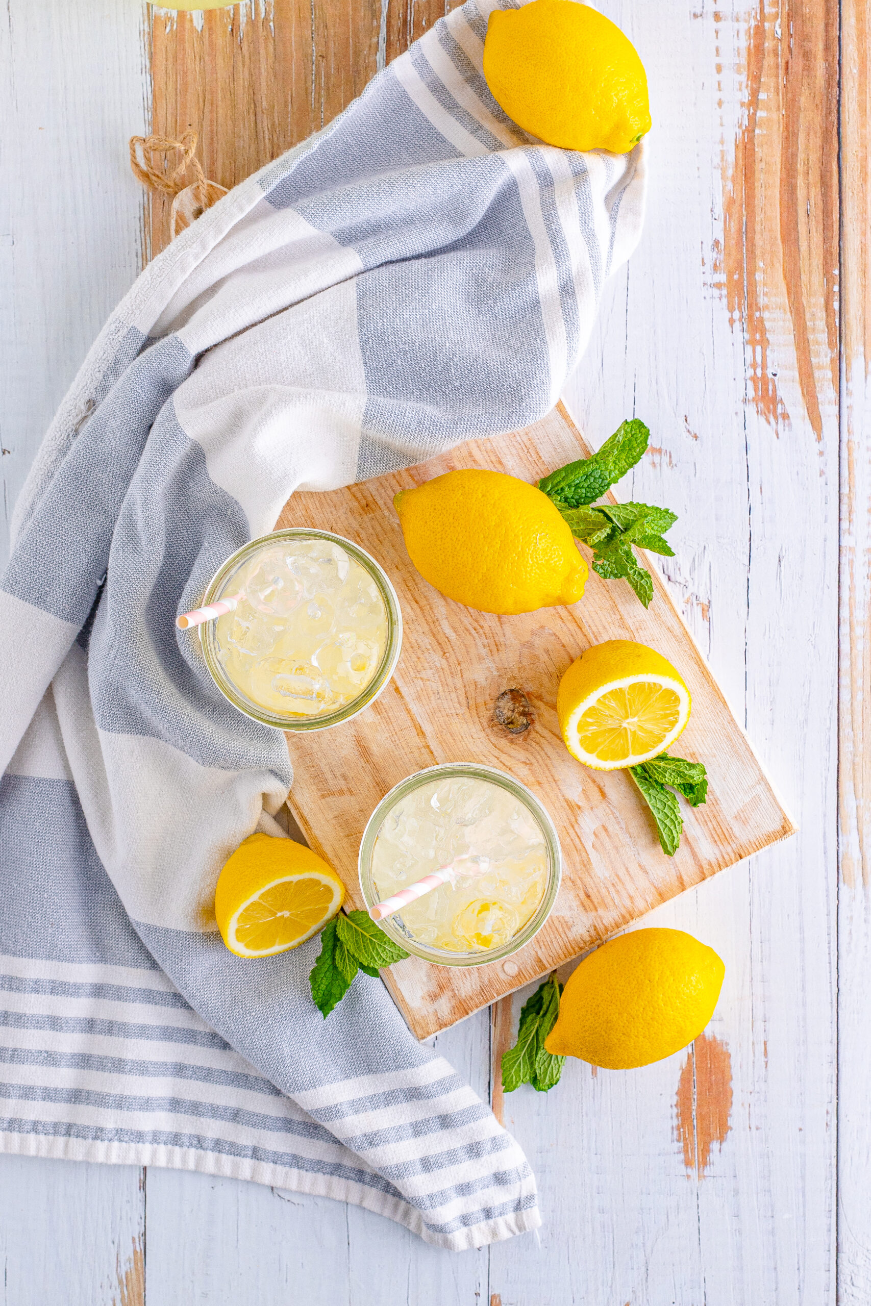 Overhead view of Homemade Lemonade in two mason jars garnished with lemon slices on a wooden cutting board.
