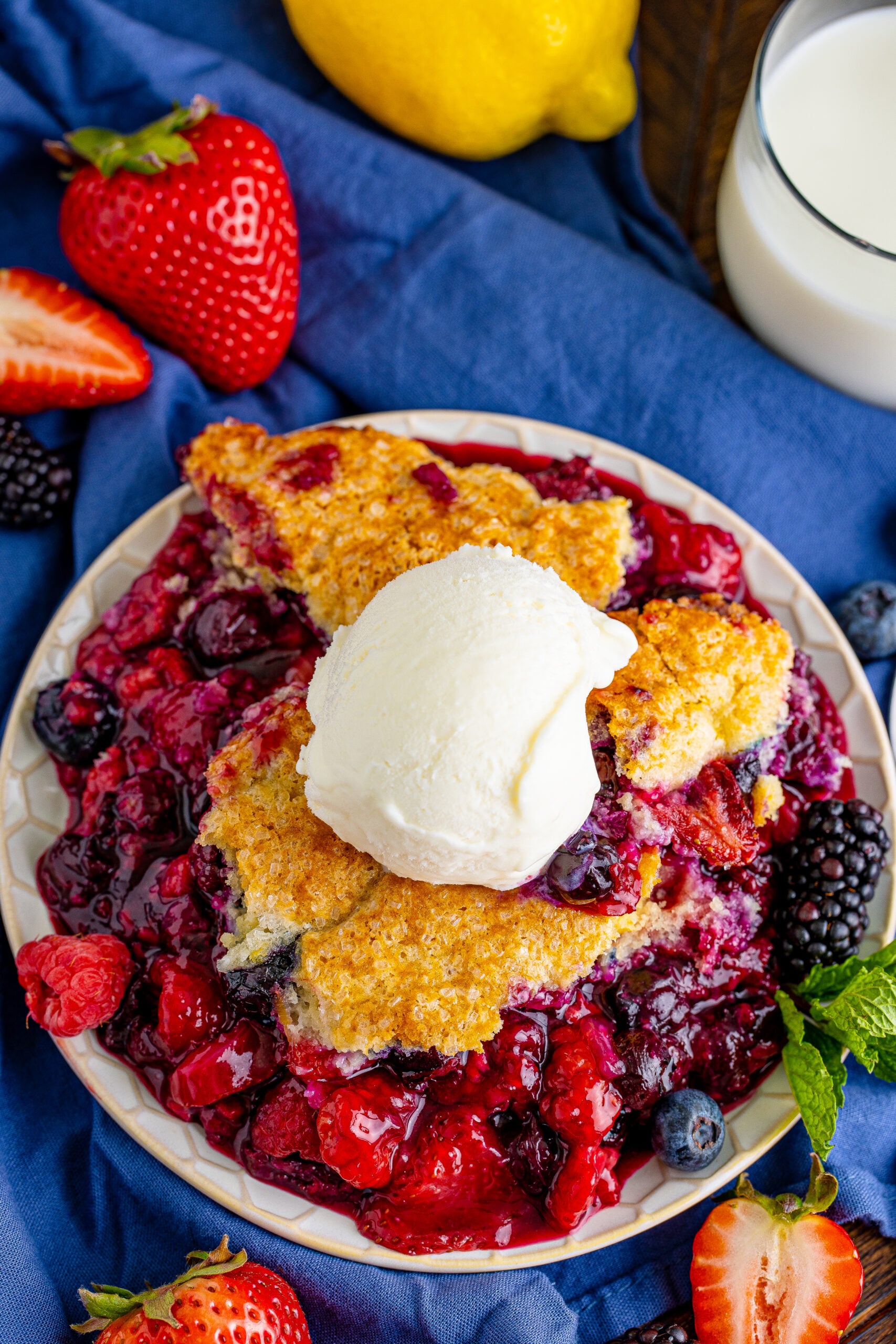 Overhead view of Mixed Berry Cobbler on a white dish served with a scoop of vanilla ice cream.