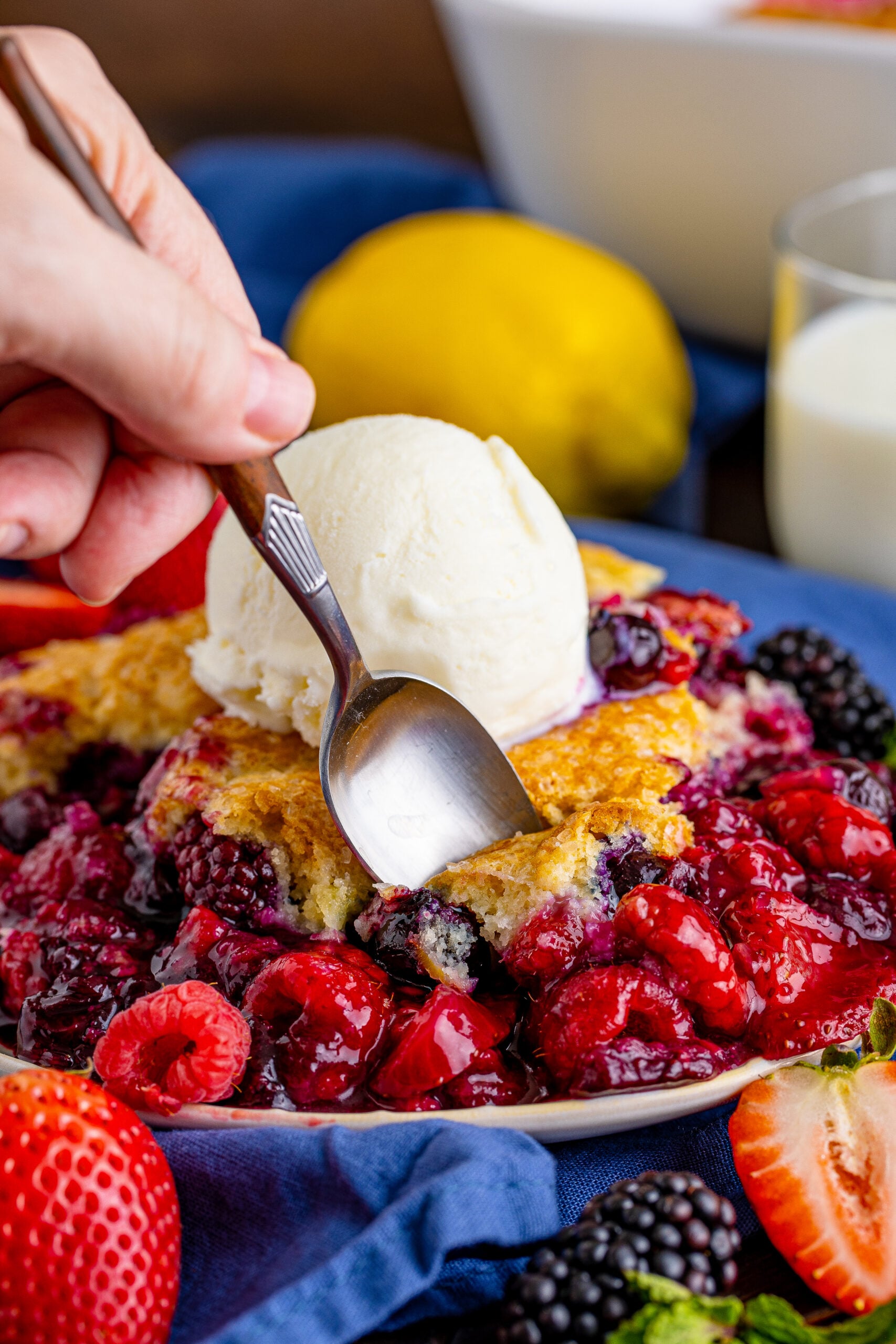 Front view of Mixed Berry Cobbler on a white dish served with a bite being removed from a silver spoon.