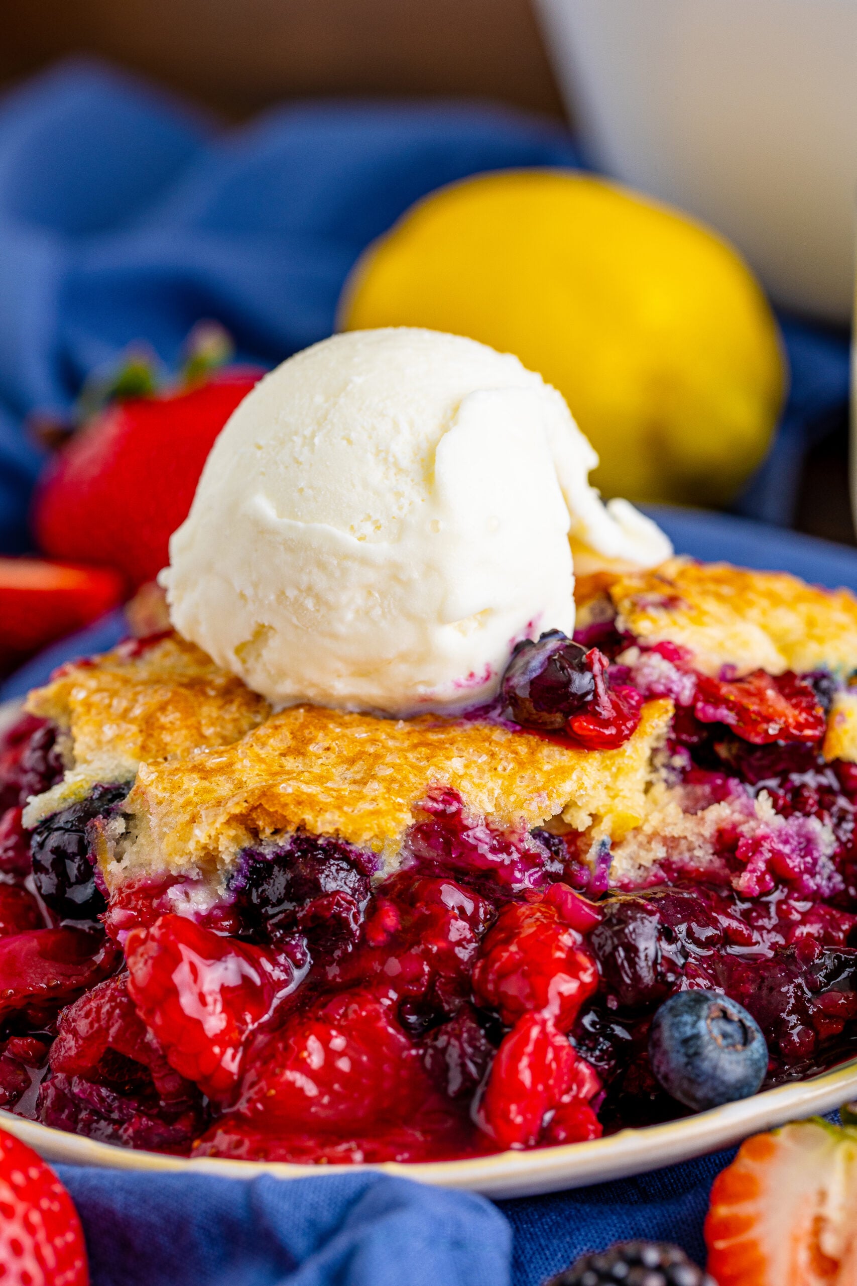 Close up view of Mixed Berry Cobbler on a white dish served with a scoop of vanilla ice cream.