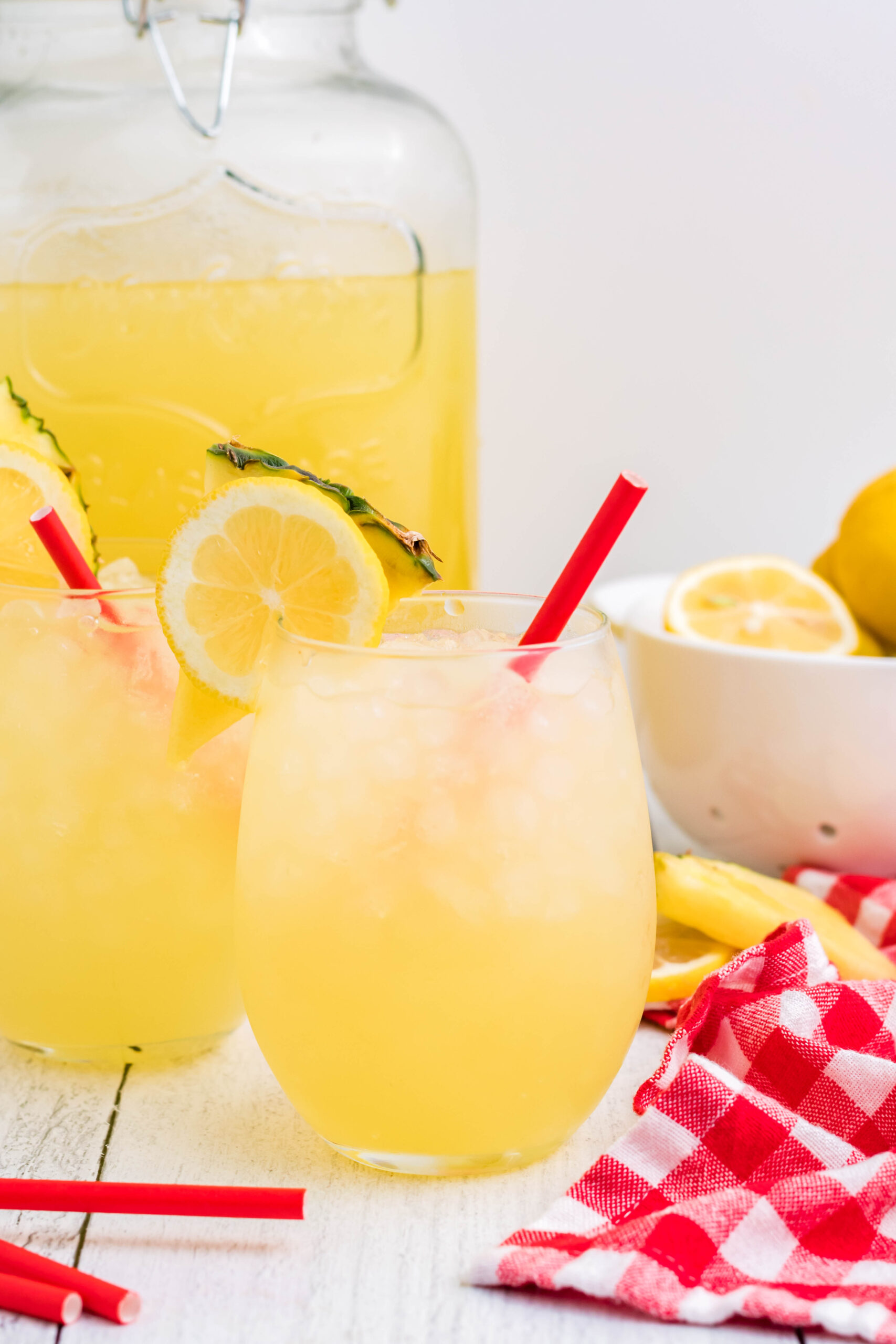 Front view of two glasses of Pineapple Vodka Lemonade garnished with a lemon and pineapple slice. 
