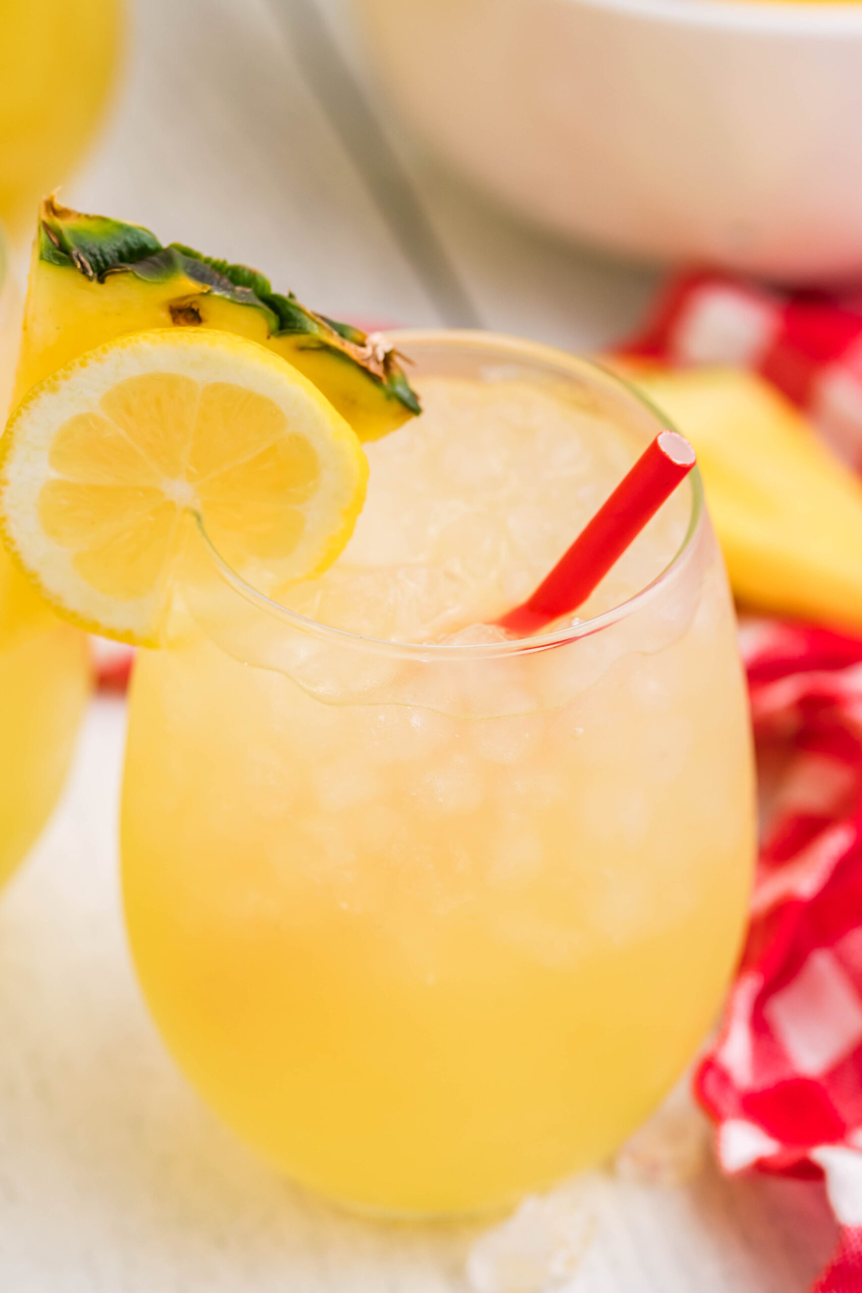 Close up view of two glasses of Pineapple Vodka Lemonade garnished with a lemon and pineapple slice. 