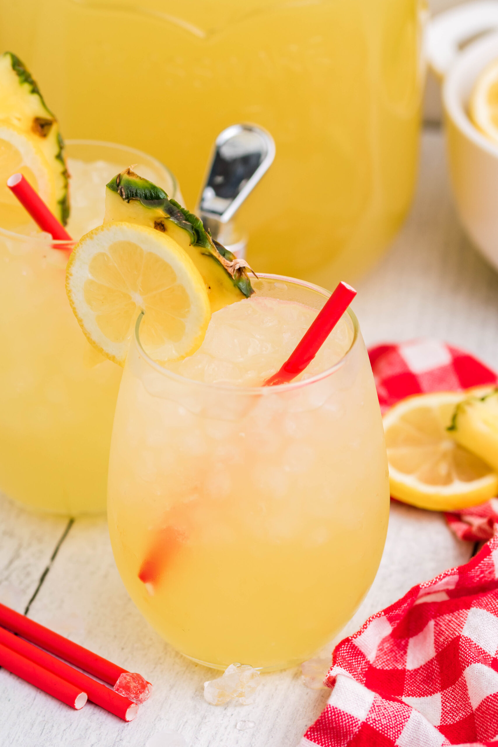 Front view of two glasses of Pineapple Vodka Lemonade garnished with a lemon and pineapple slice. 