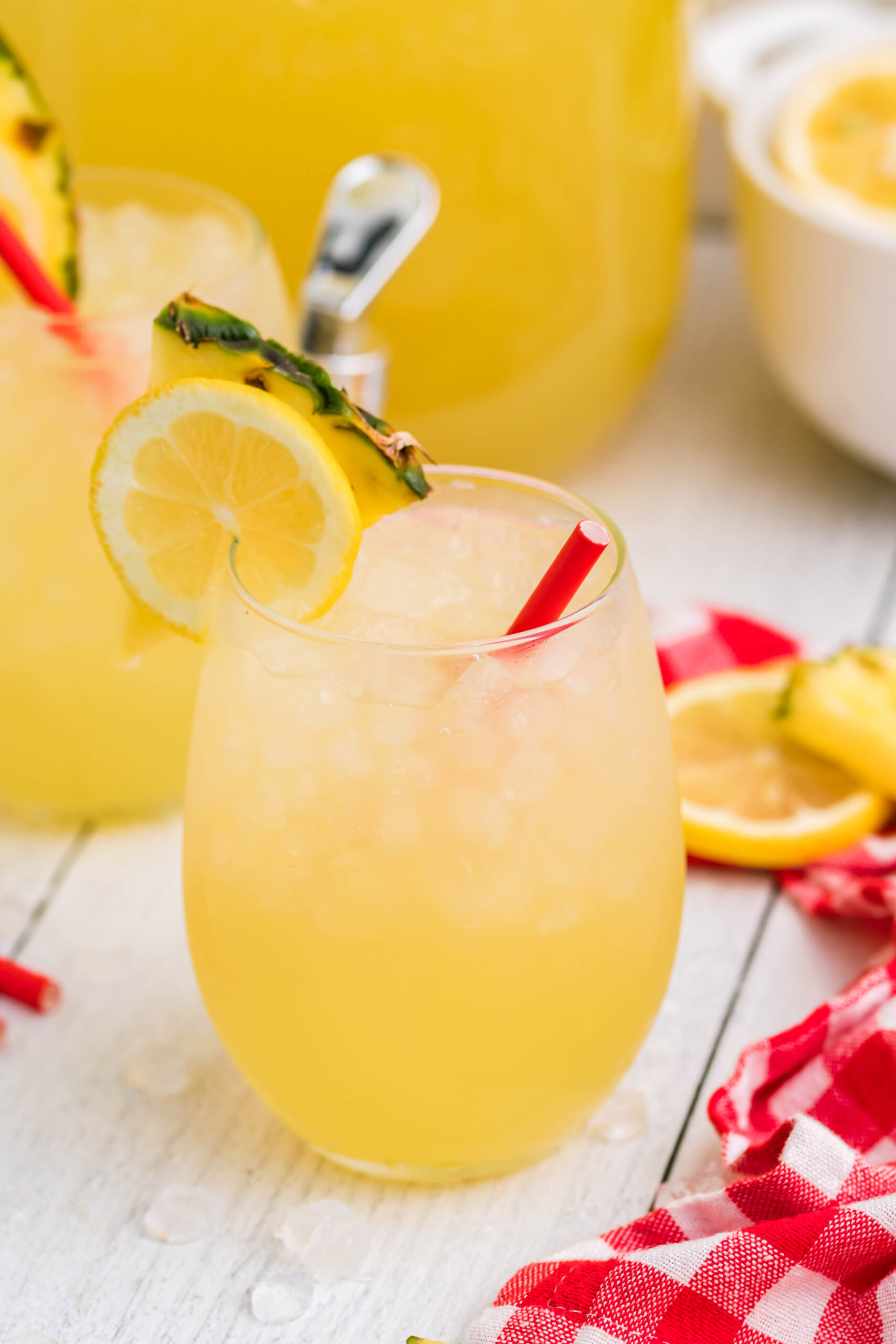Front view of two glasses of Pineapple Vodka Lemonade garnished with a lemon and pineapple slice. 