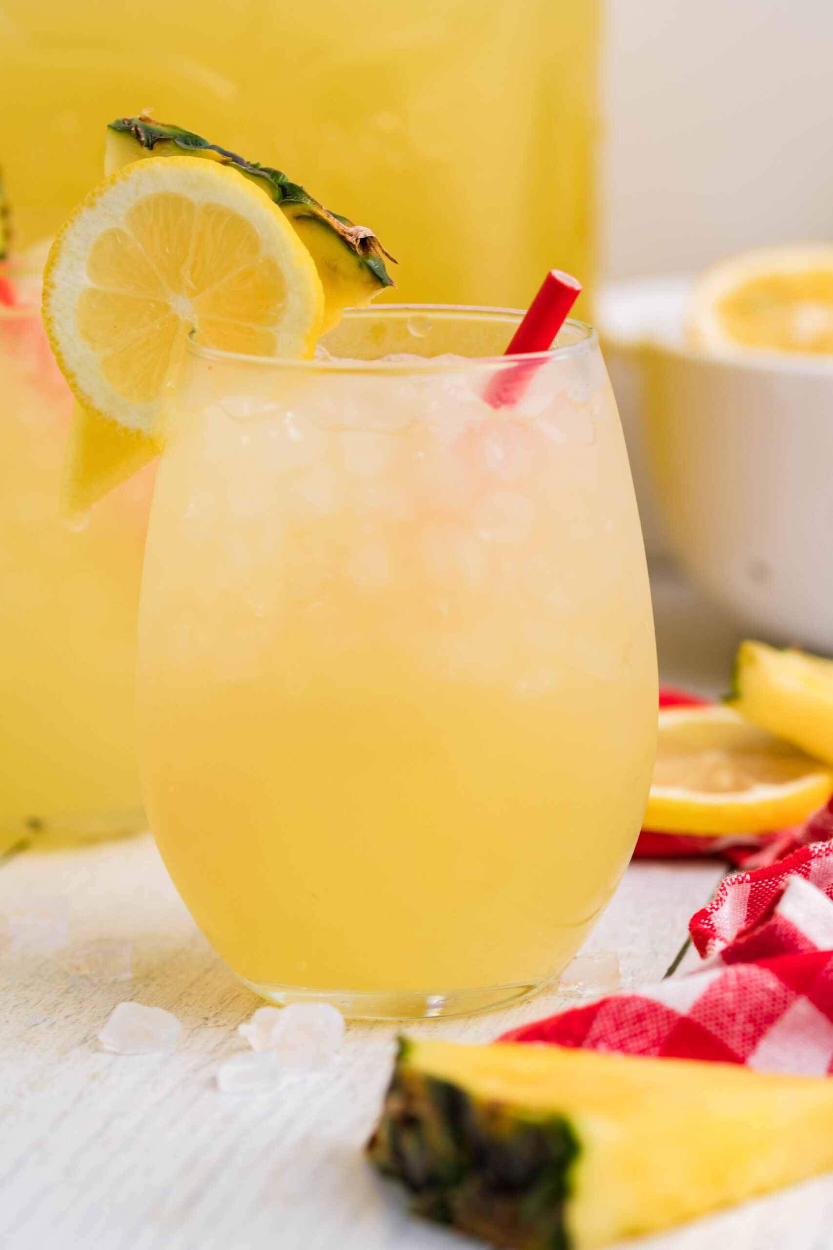 Front view of two glasses of Pineapple Vodka Lemonade garnished with a lemon and pineapple slice. 