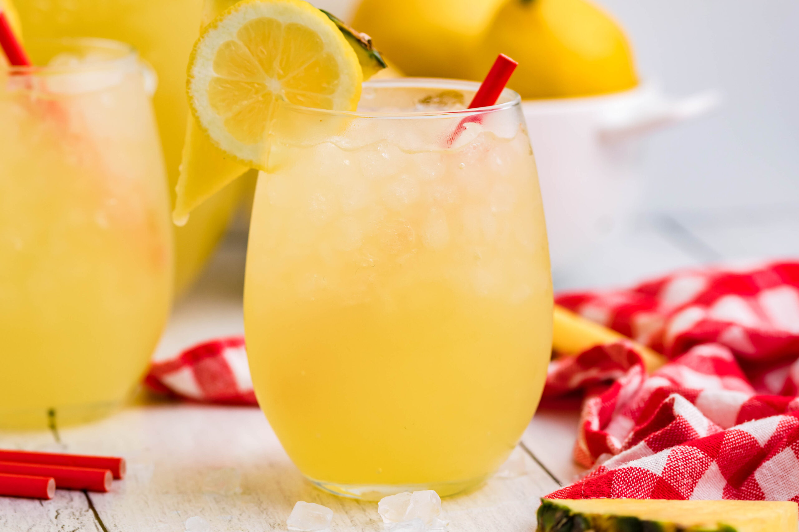 Front view of two glasses of Pineapple Vodka Lemonade garnished with a lemon and pineapple slice. 