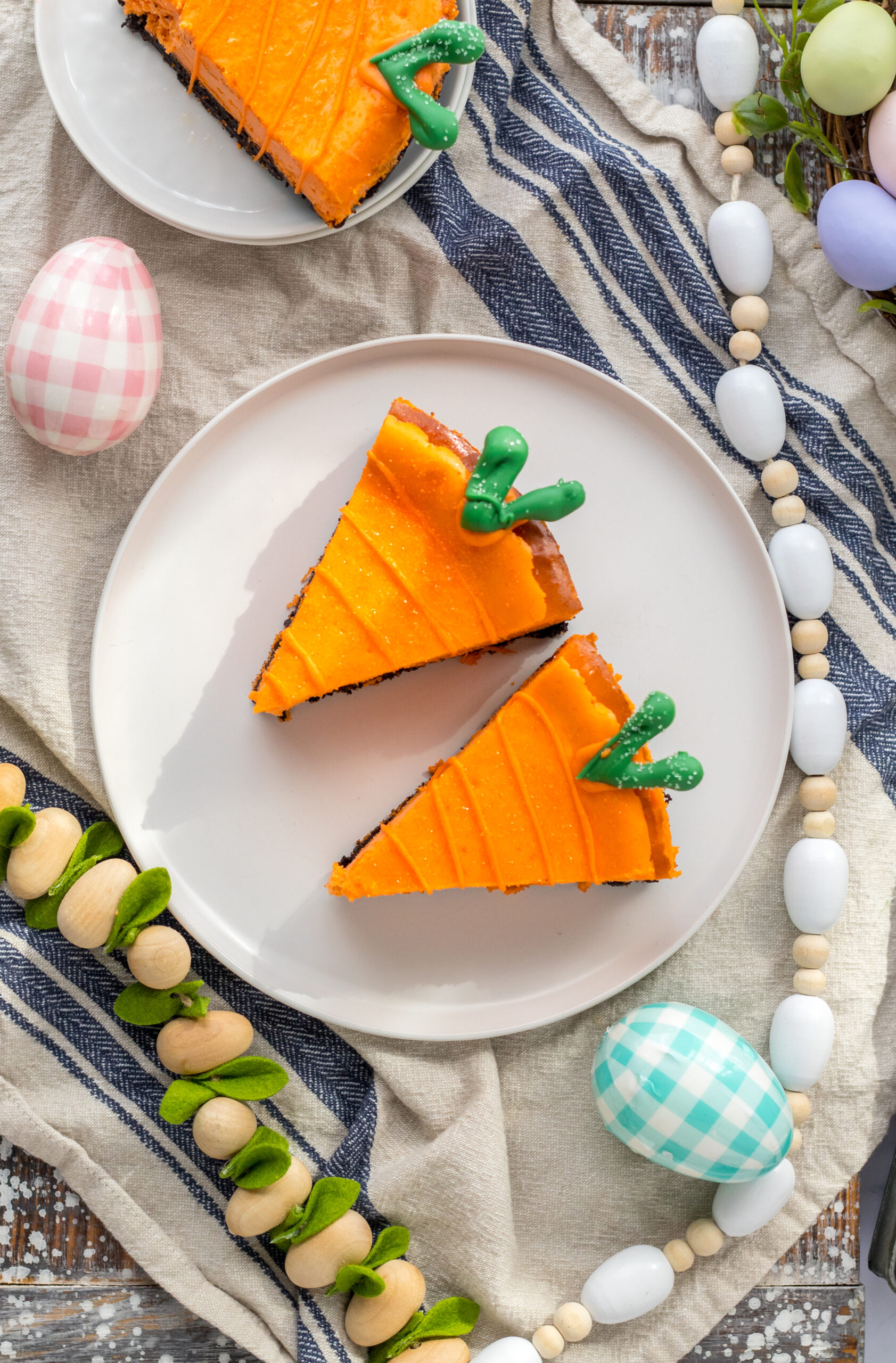 Three pieces of Cheesecake Carrots on two white plates with a blue and white linen in the background.