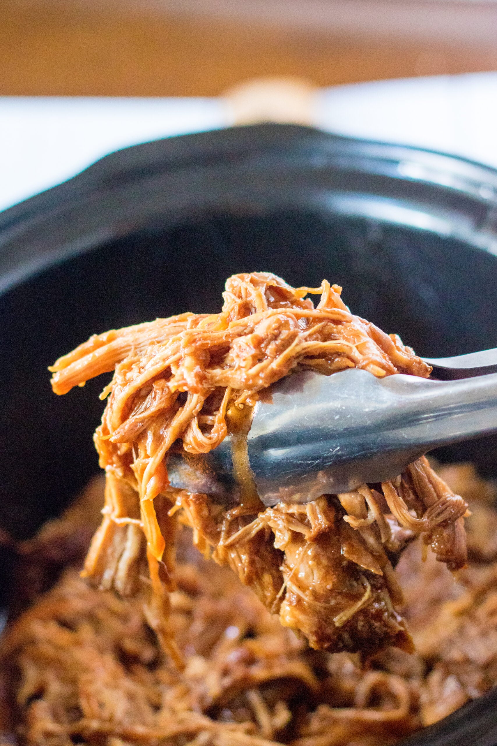 Front view of silver tongs holding a serving of Slow Cooker Cola Pulled Pork.