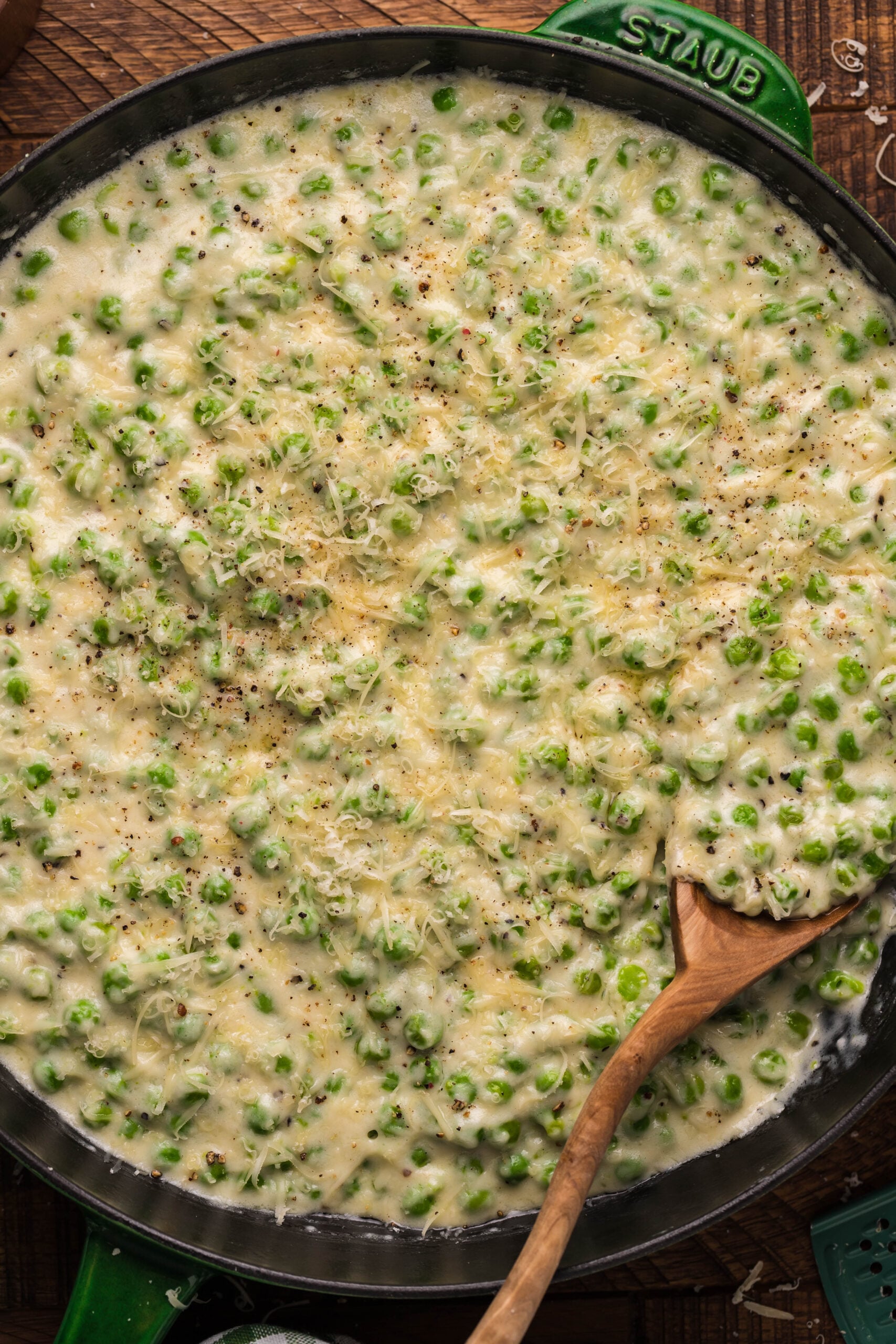 Close up shot of creamed peas in a green and black cast iron skillet with a wooden spoon. 