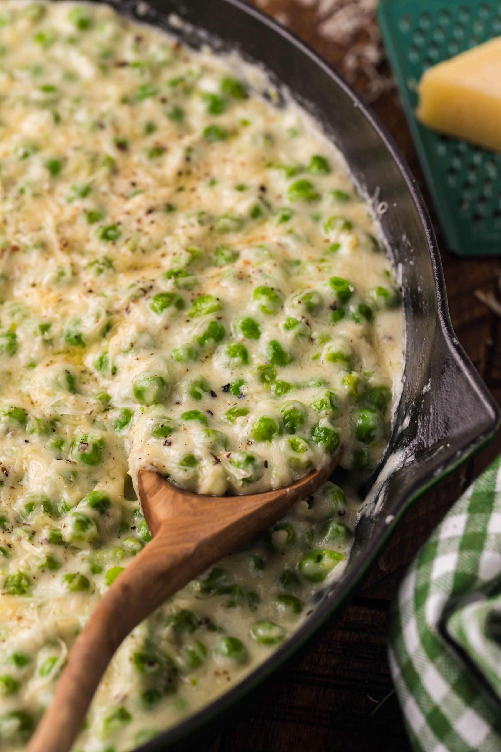 Close up shot of Creamed Peas in a black and green cast iron skillet with a wood spoon. 