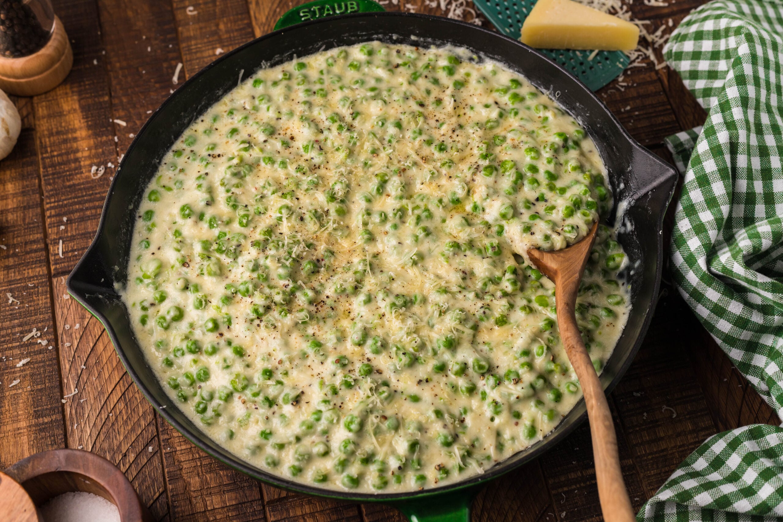 Creamed Peas in a black and green cast iron skillet with a wood spoon. 
