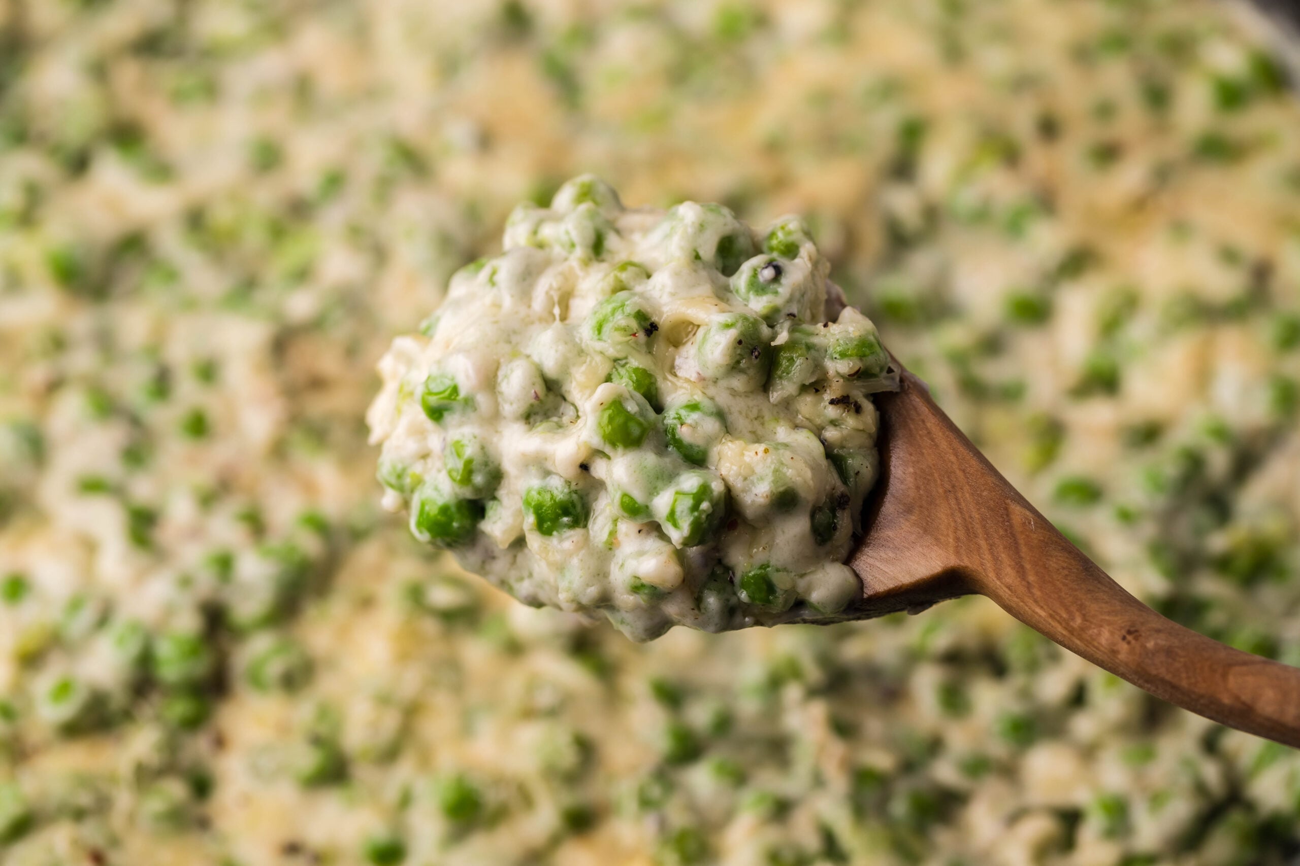 A wooden spoon removing creamed peas from a cast iron skillet. 