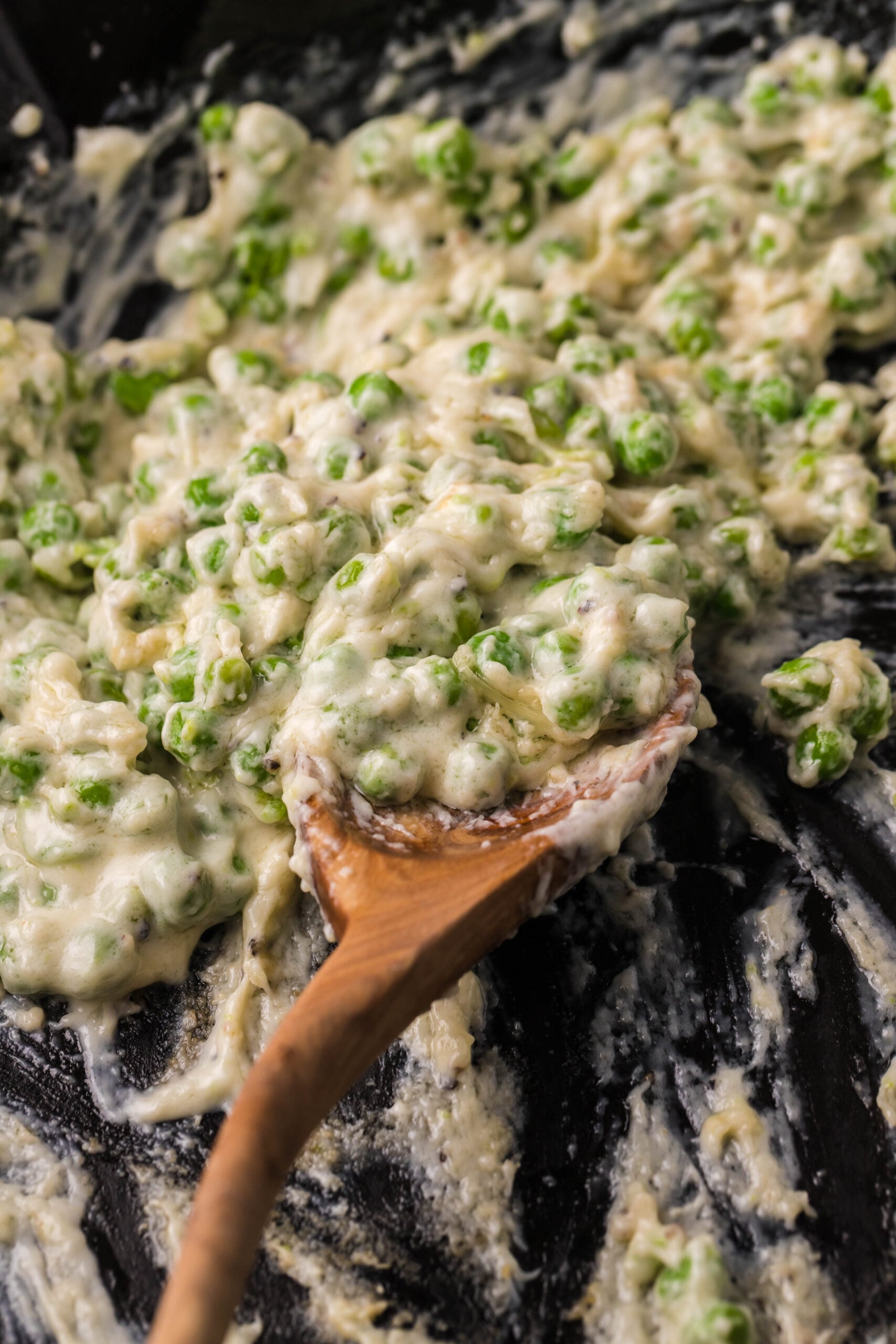 A wooden spoon removing creamed peas from a cast iron skillet. 