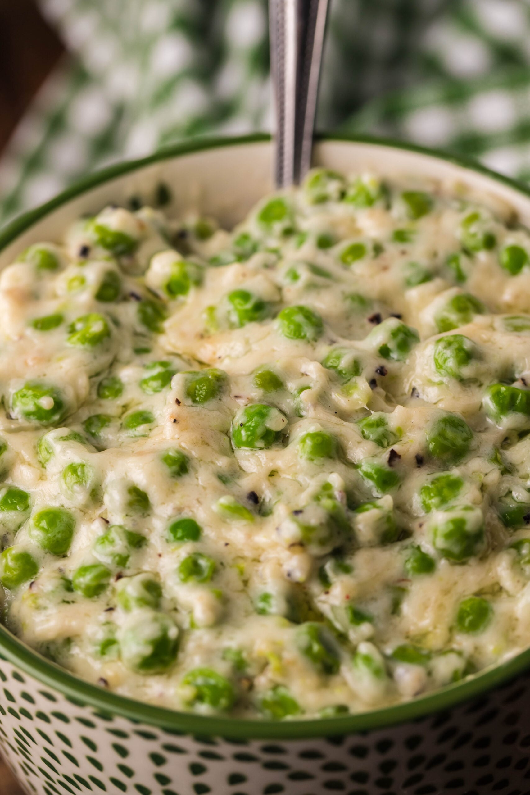 Close up shot of creamed peas in a green and white bowl. 