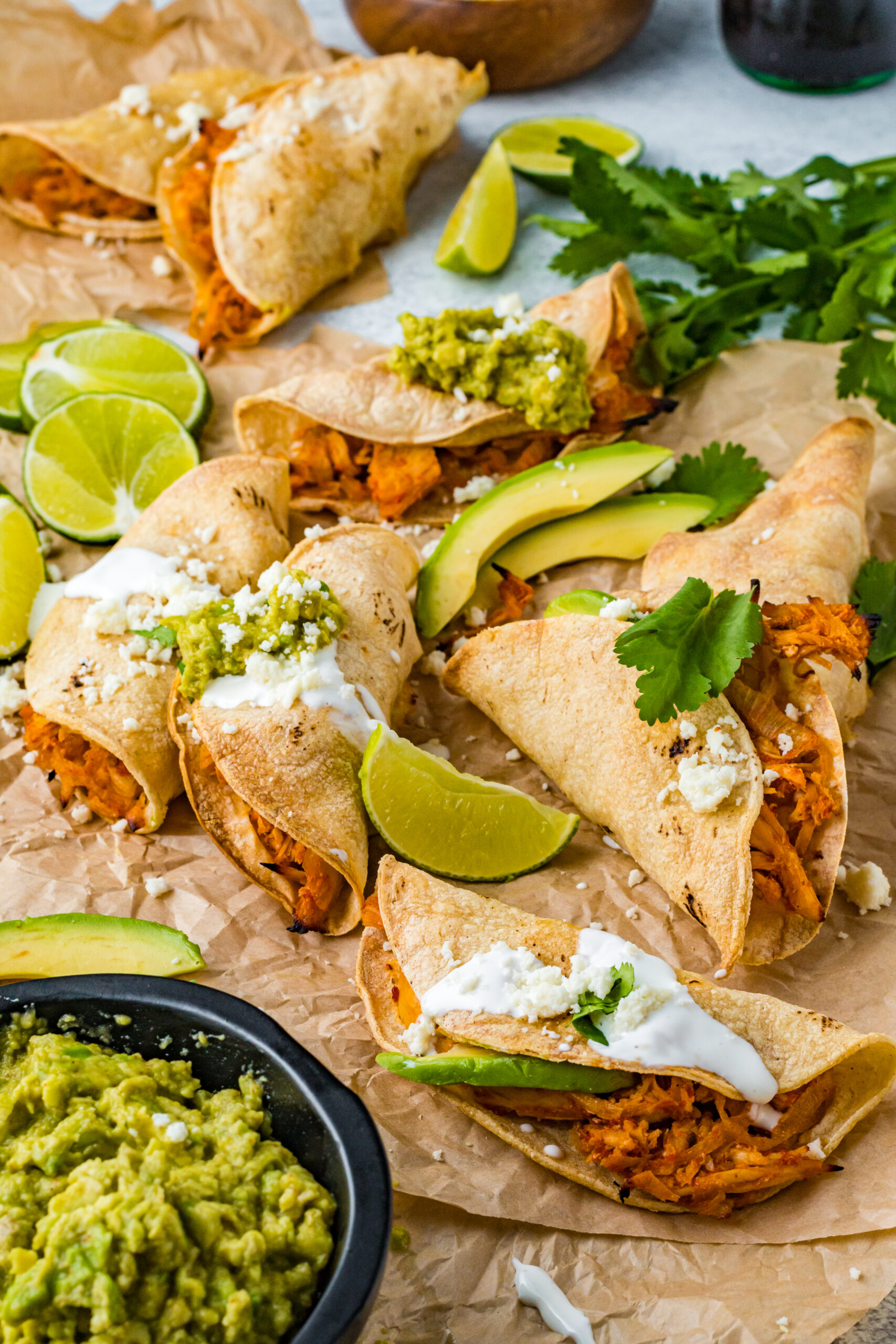 Front view of Crispy Tinga Tacos on a piece of parchment paper surrounded by lime and avocado slices.