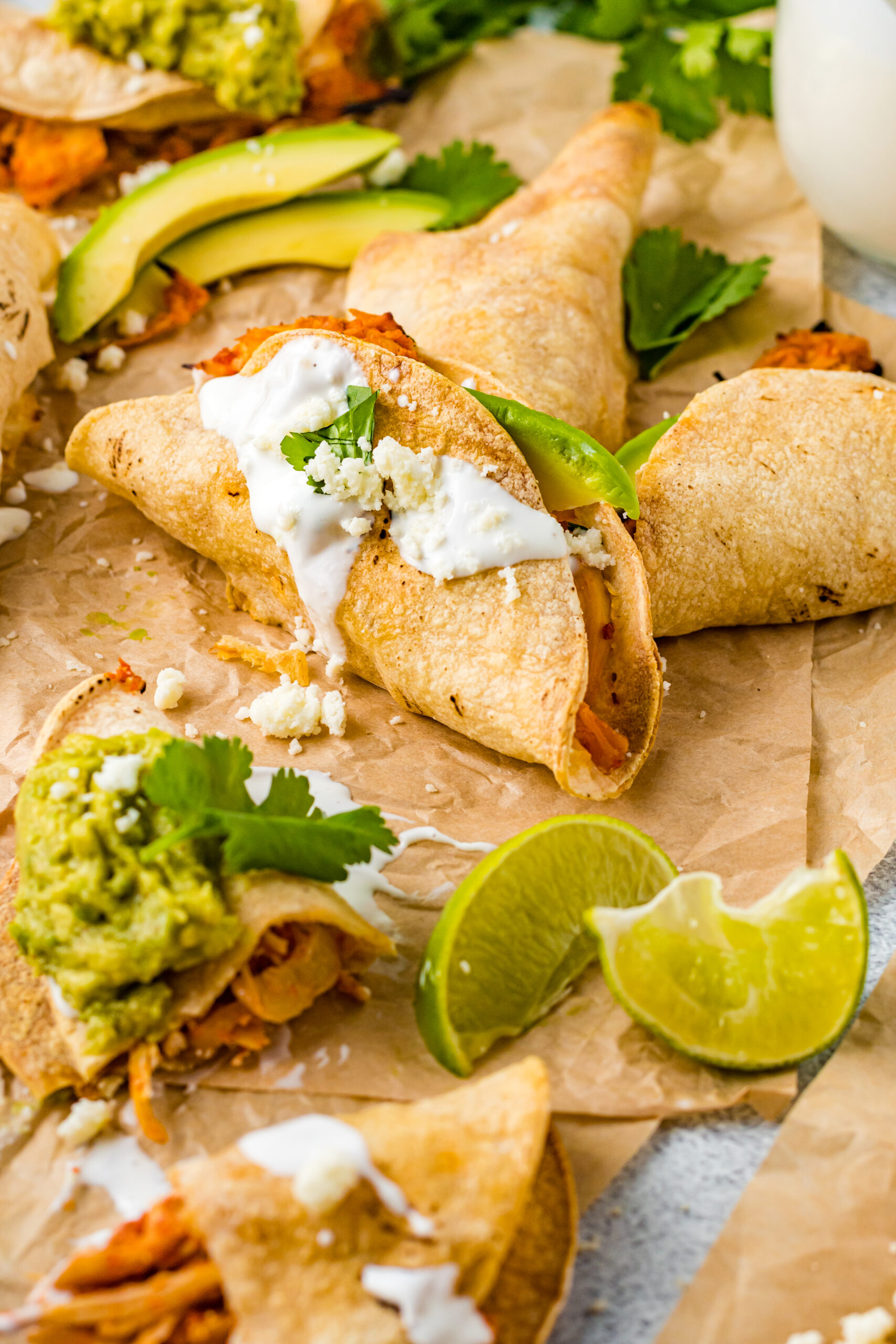 Front view of Crispy Tinga Tacos on a piece of parchment paper surrounded by lime and avocado slices.