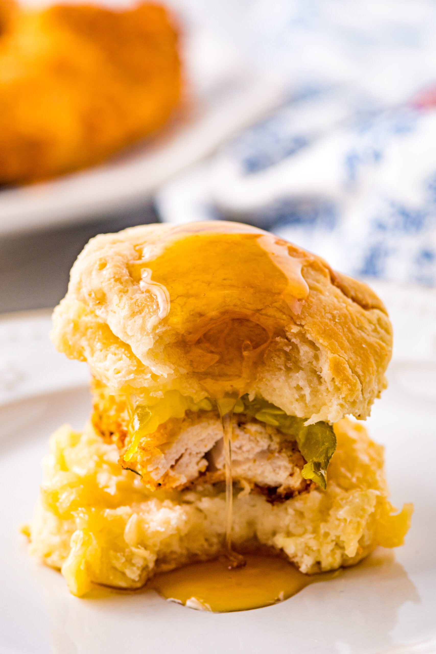 Front view of Honey Butter Chicken Biscuit on a white plate with a bite removed.