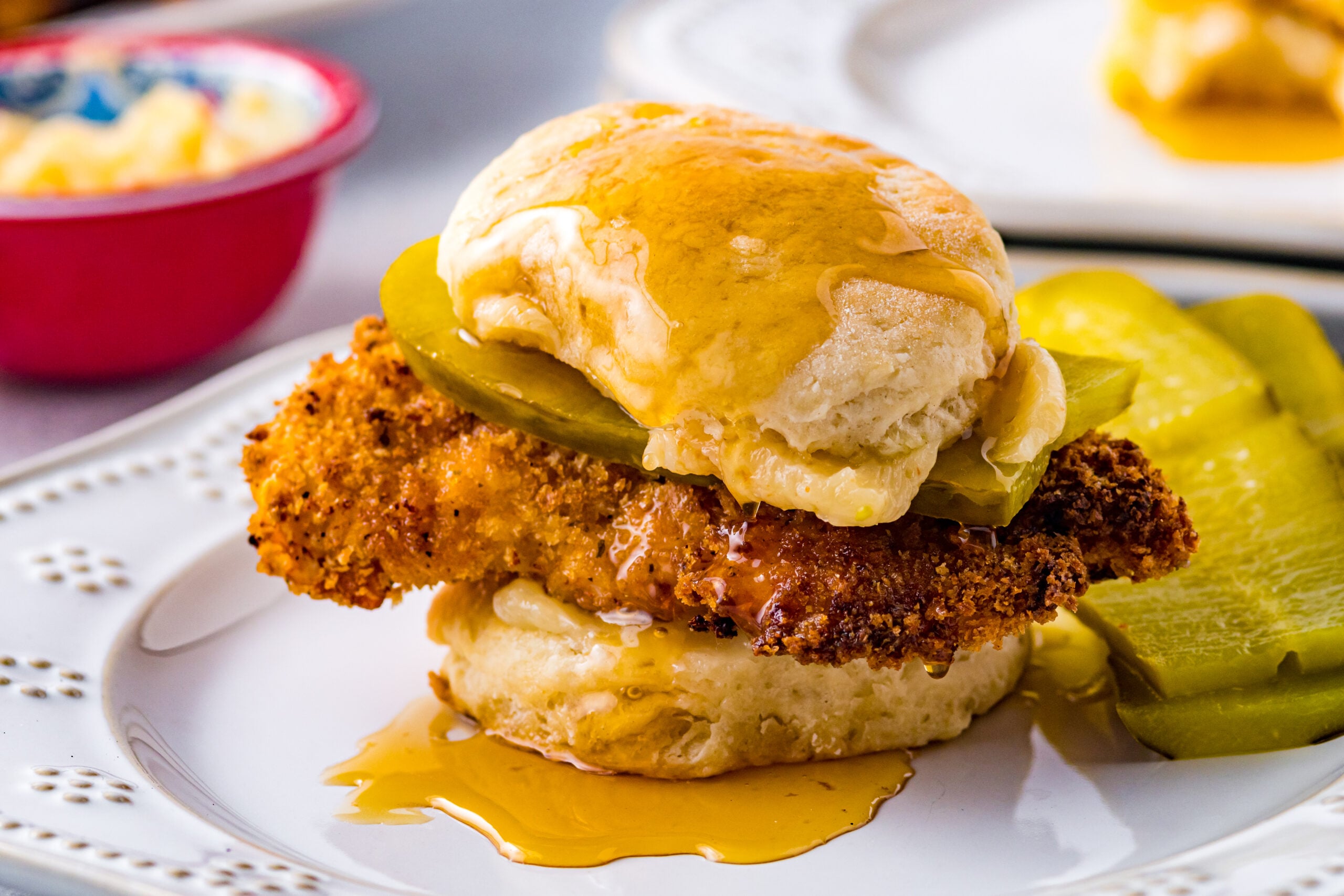 Front view of Honey Butter Chicken Biscuit on a white plate served with two pickle slices.
