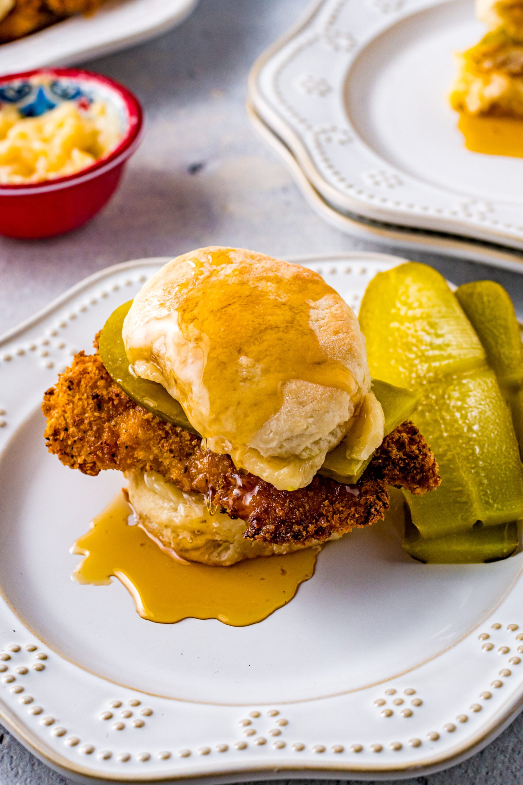 Front view of Honey Butter Chicken Biscuit on a white plate served with two pickle slices.