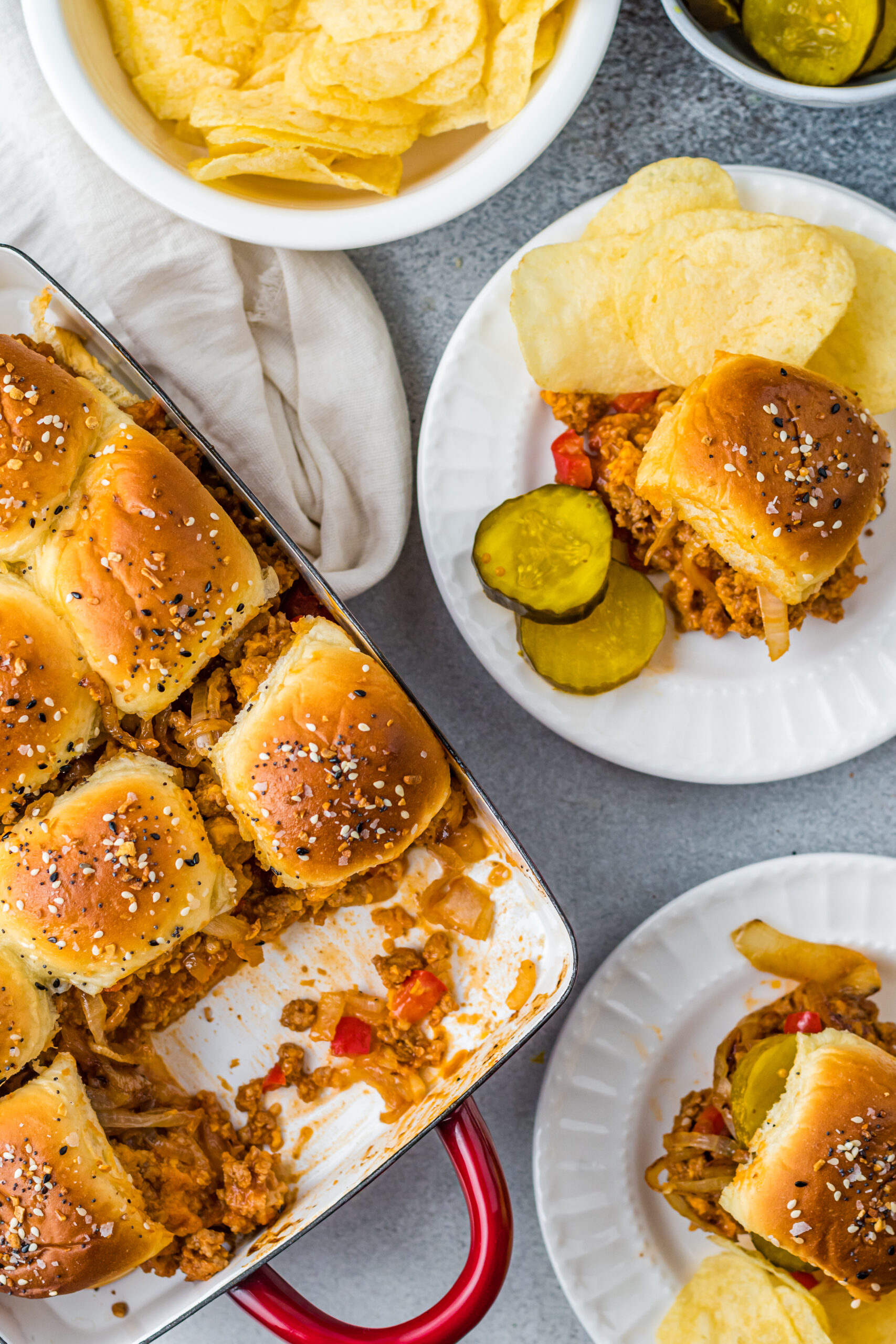 Overhead view of Cheesy Chicken Sloppy Joe Sliders on white plates served with pickle slices and chips.