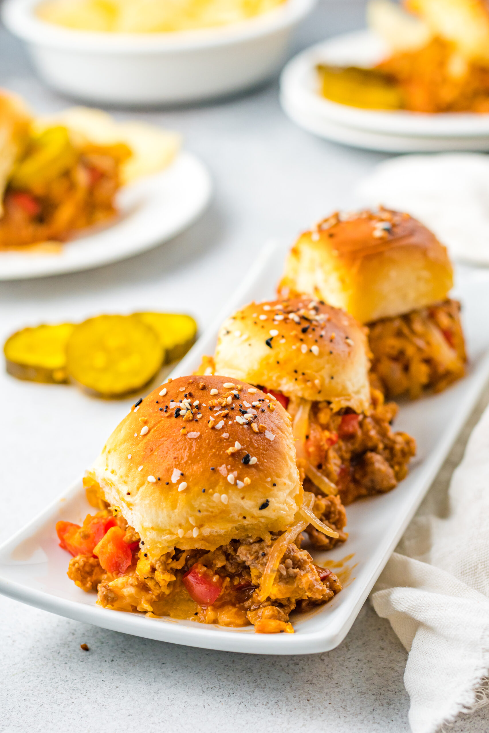 Front view of three Cheesy Chicken Sloppy Joe Sliders on a white serving dish.
