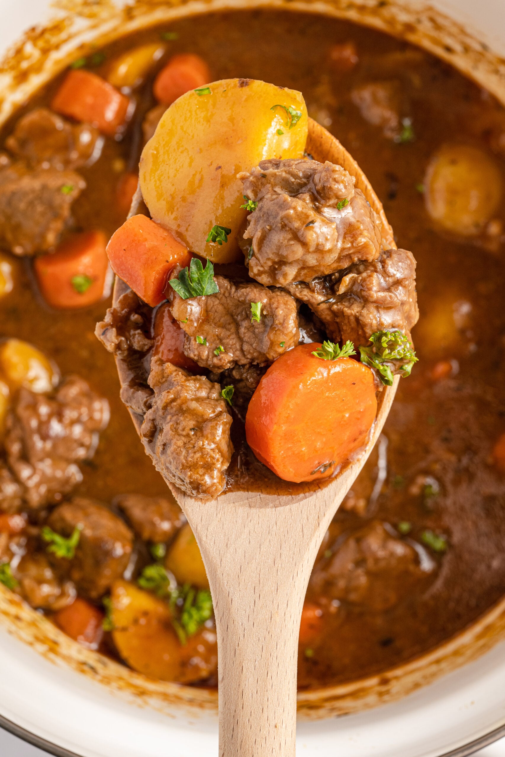 A wooden spoon holding Irish Stew over a large cooking pot.