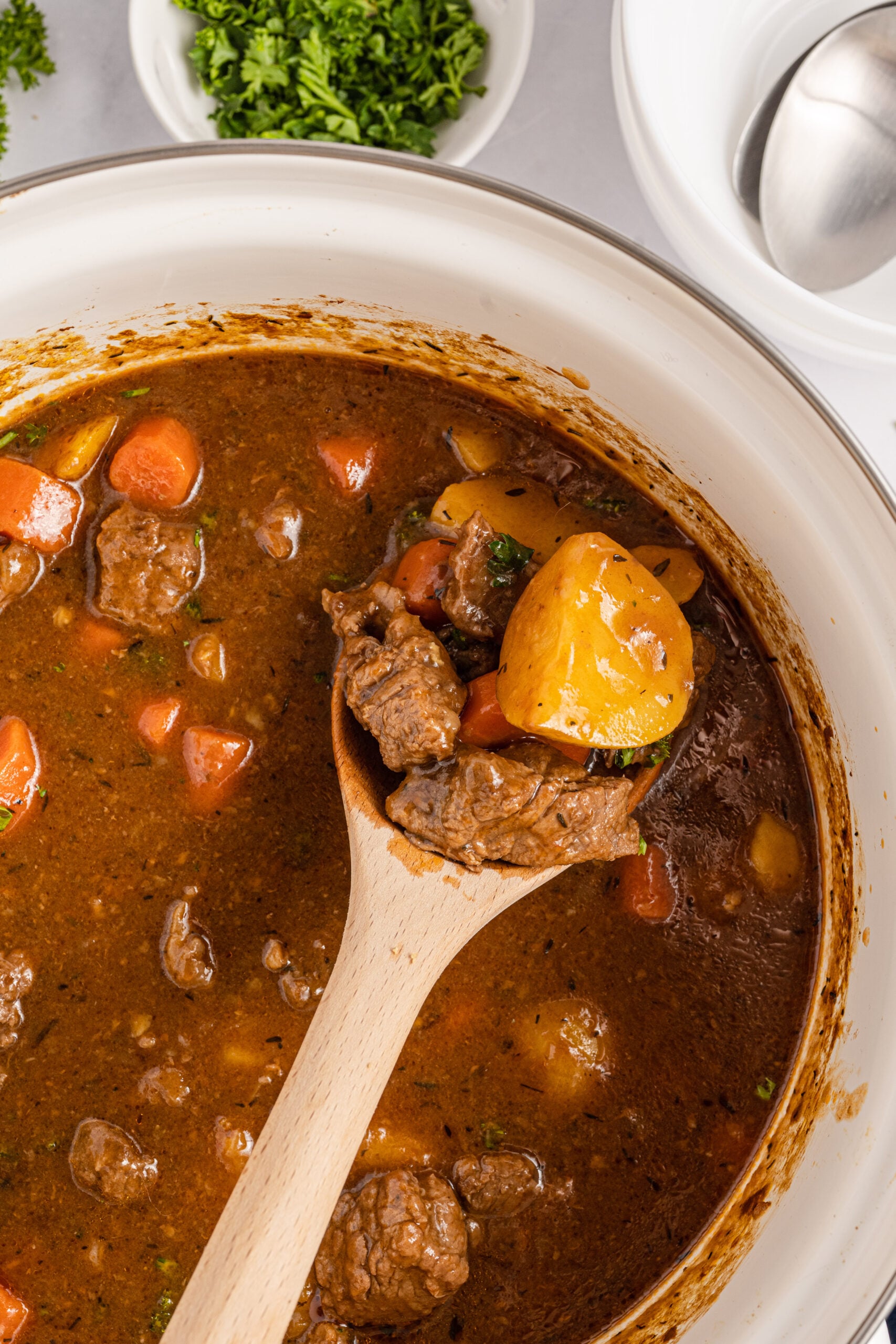 A wooden spoon removing the stew from a large cooking pot.