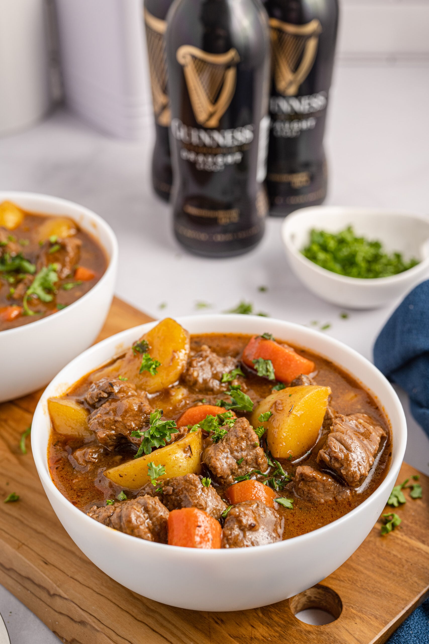 Two bowls of Irish stew sitting on a wooden board with Guinness beer bottles in the background.