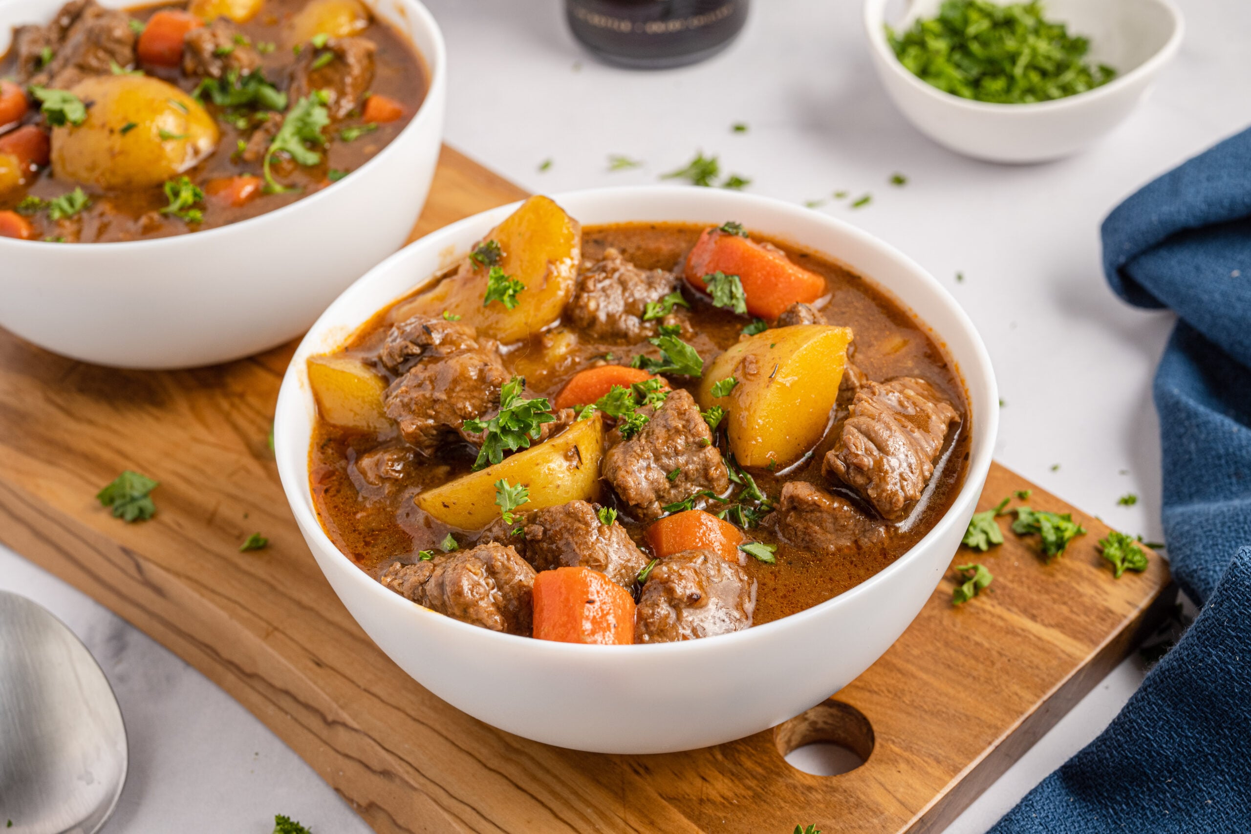 Two bowls of Irish stew sitting on a wooden board with Guinness beer bottles in the background.