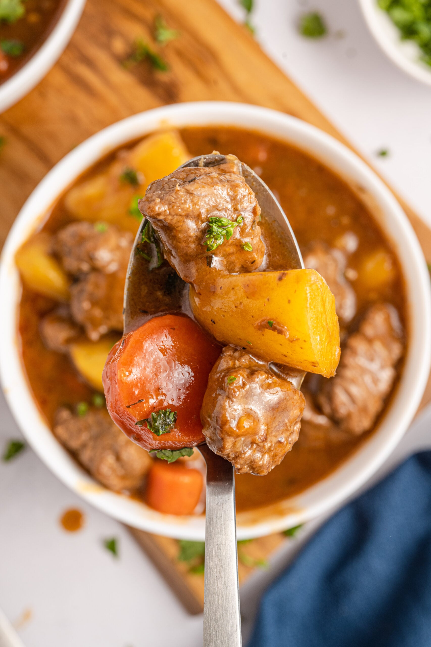 A silver spoon holding Irish Stew over a white bowl of stew.