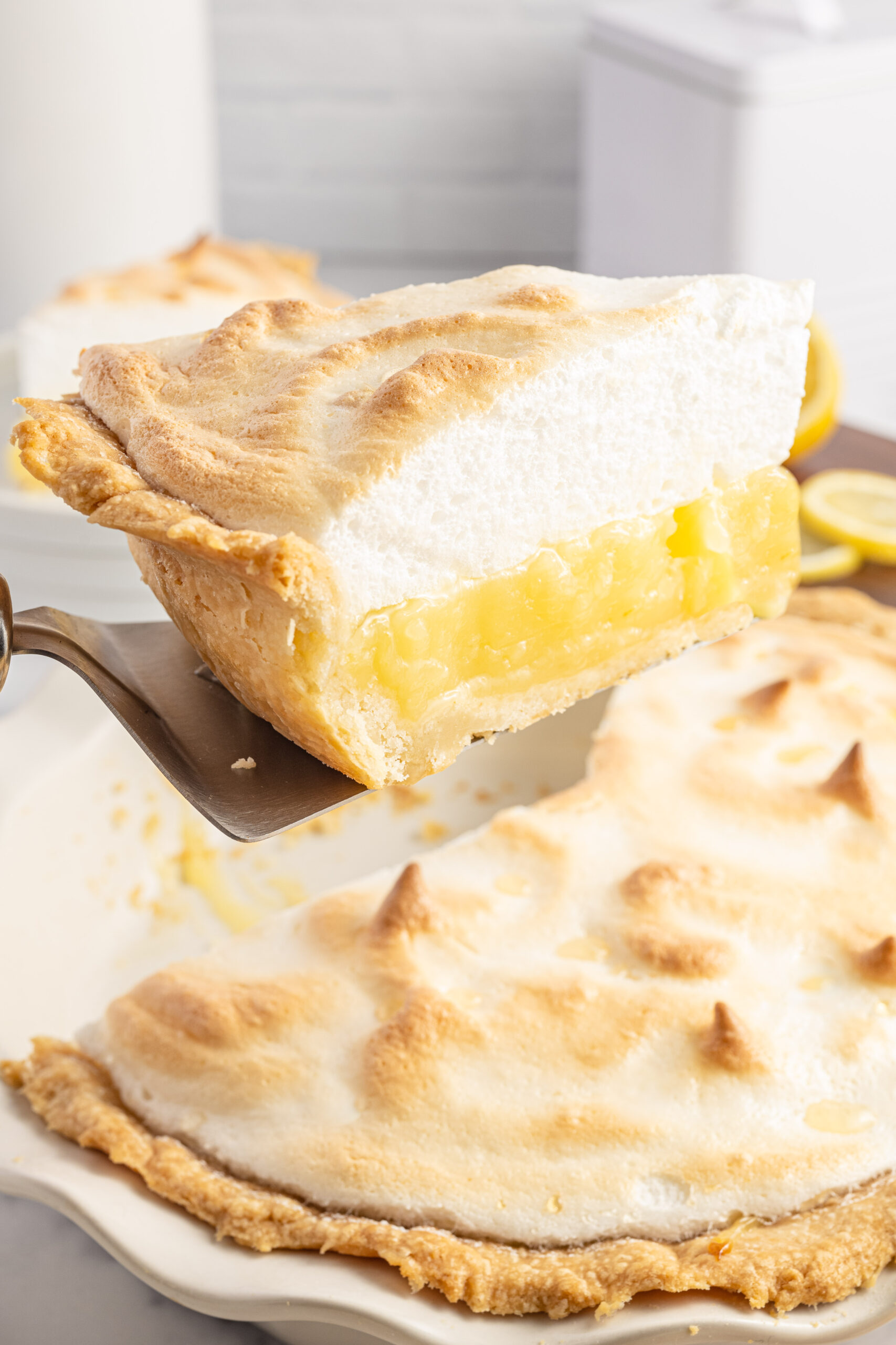 A slice of lemon pie being held up by a silver spatula. 