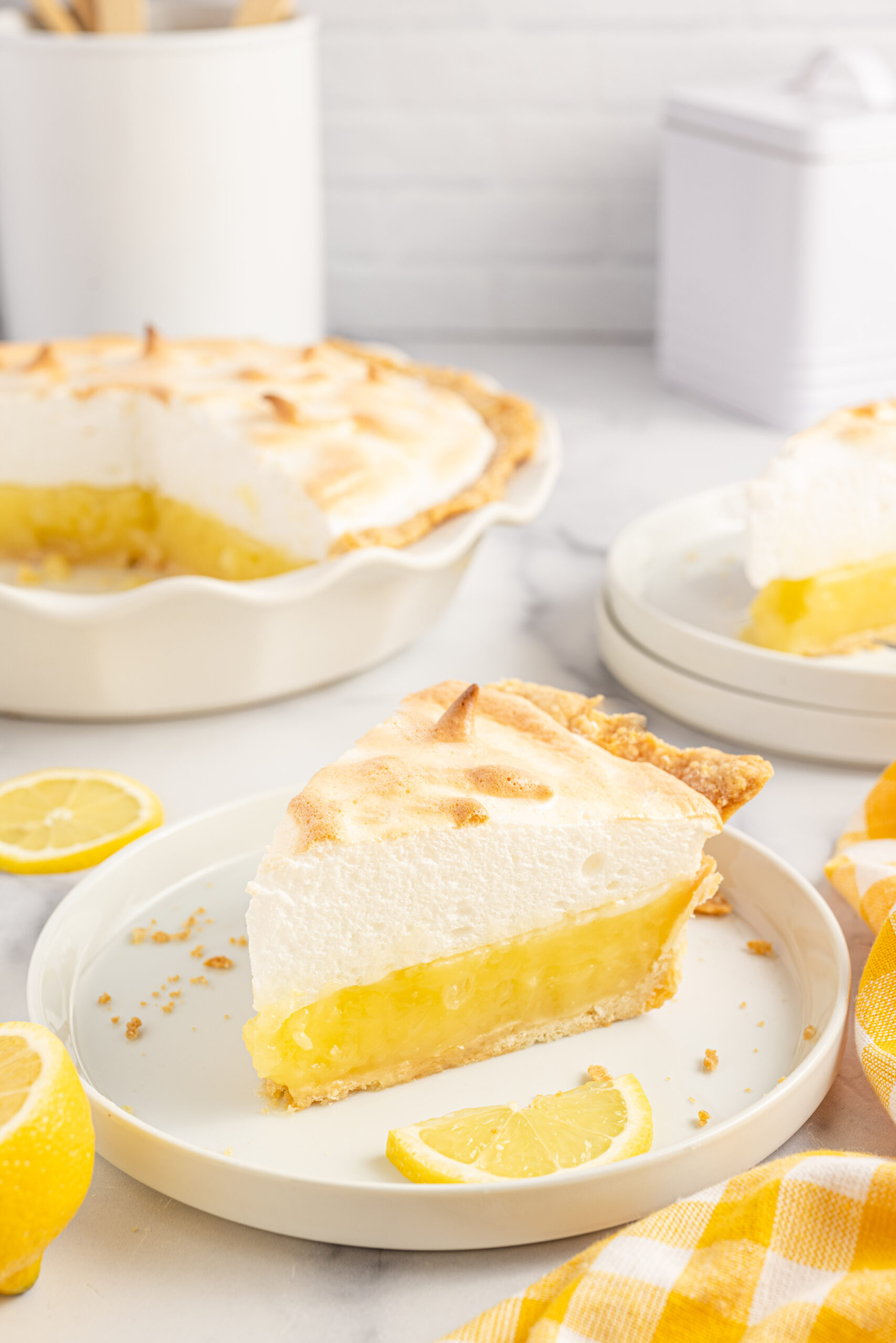 A piece of meringue pie on a white plate with fresh lemons. 