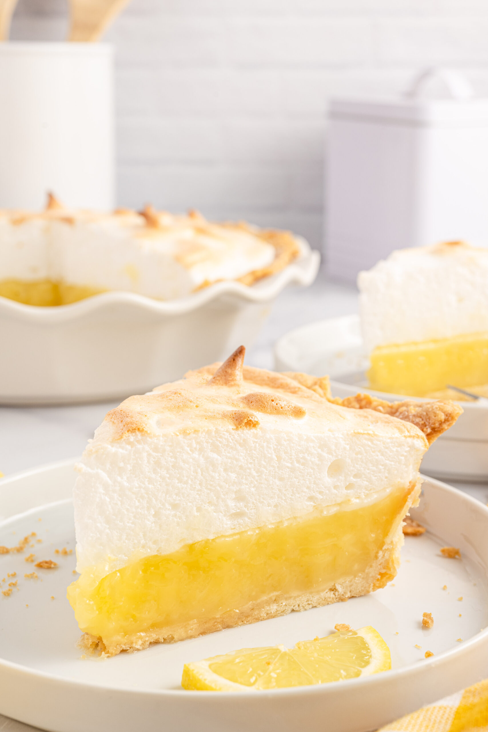 up close view of a piece of the lemon meringue pie on a white plate with fresh sliced lemons. 
