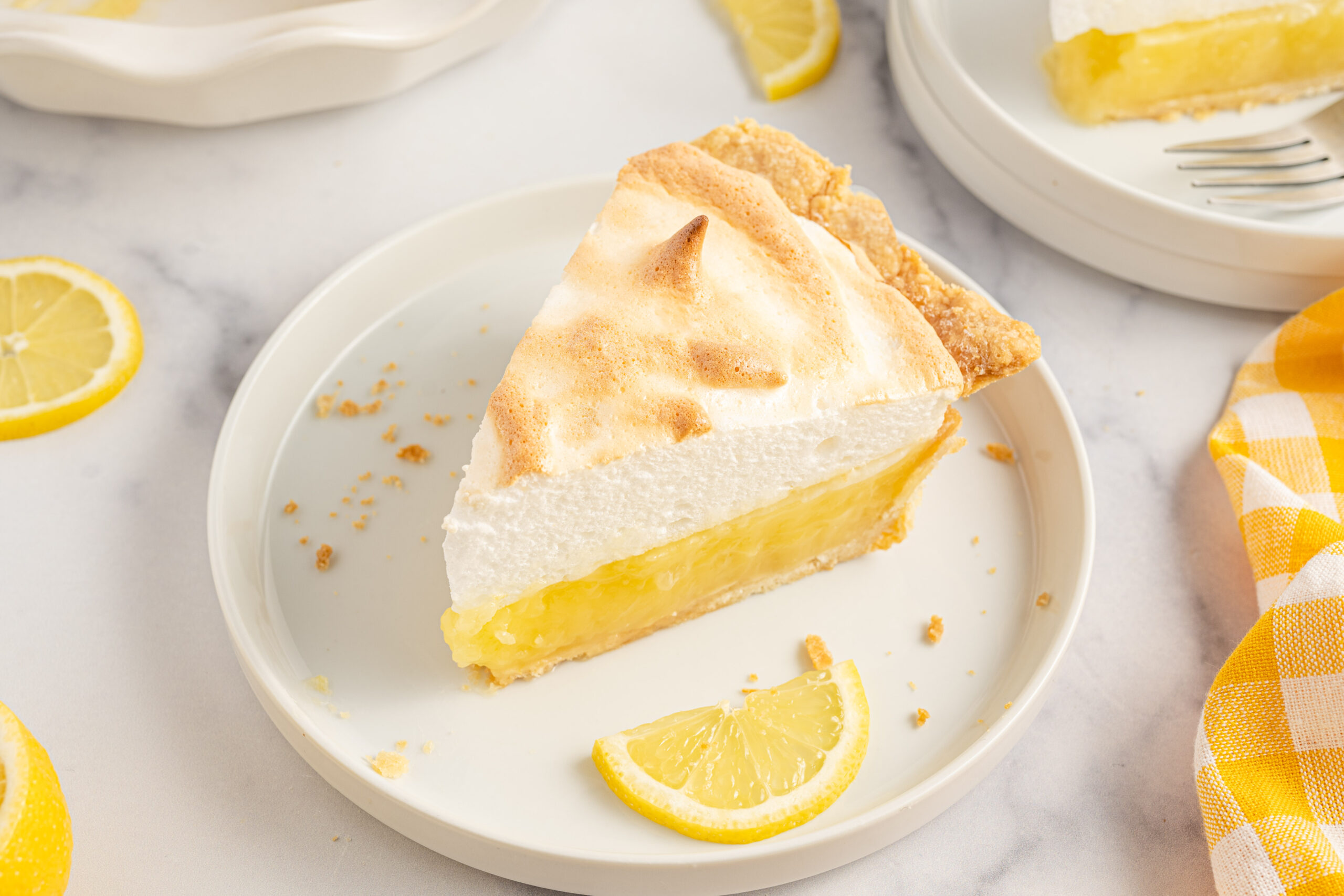 A piece of meringue pie on a white plate with fresh lemons. 