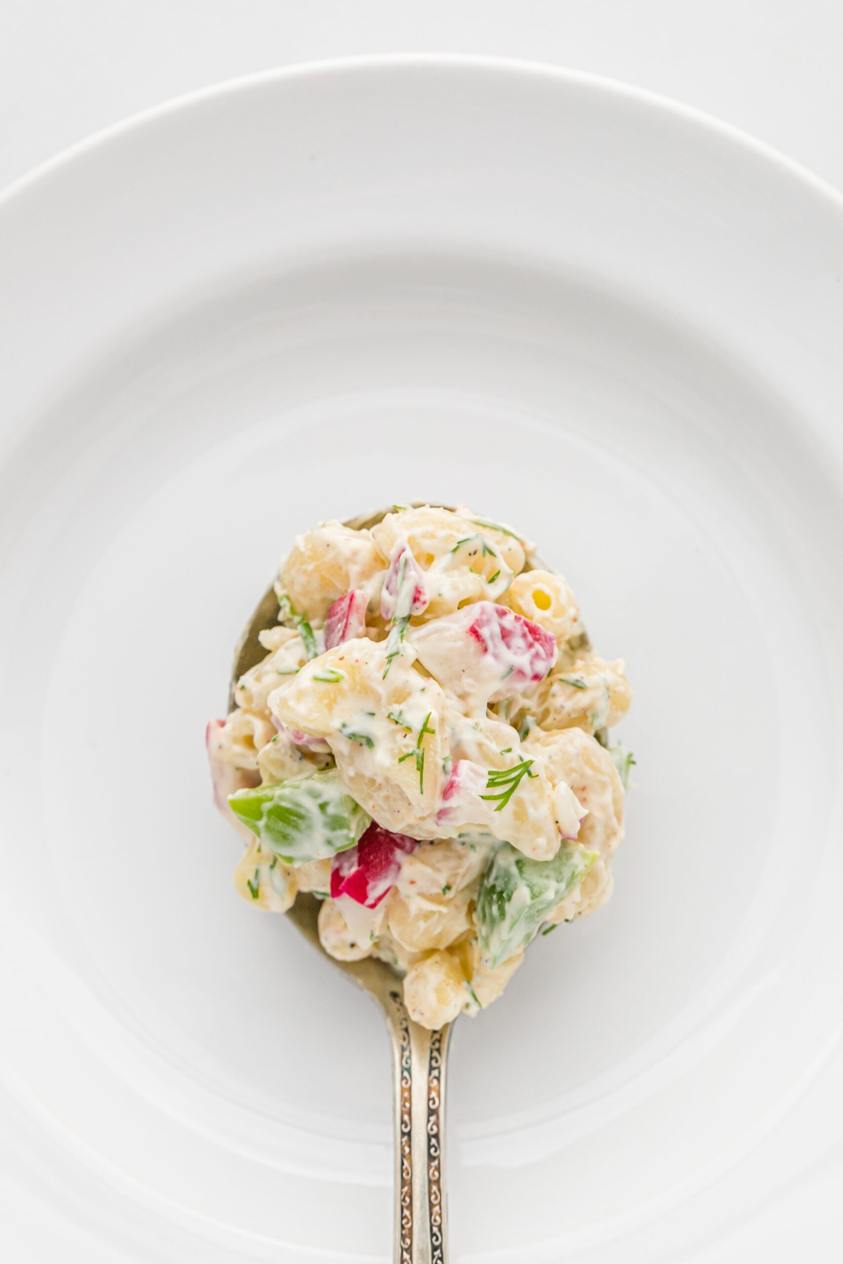 Overhead view of a bite of Macaroni Dill Pasta Salad on a silver spoon.