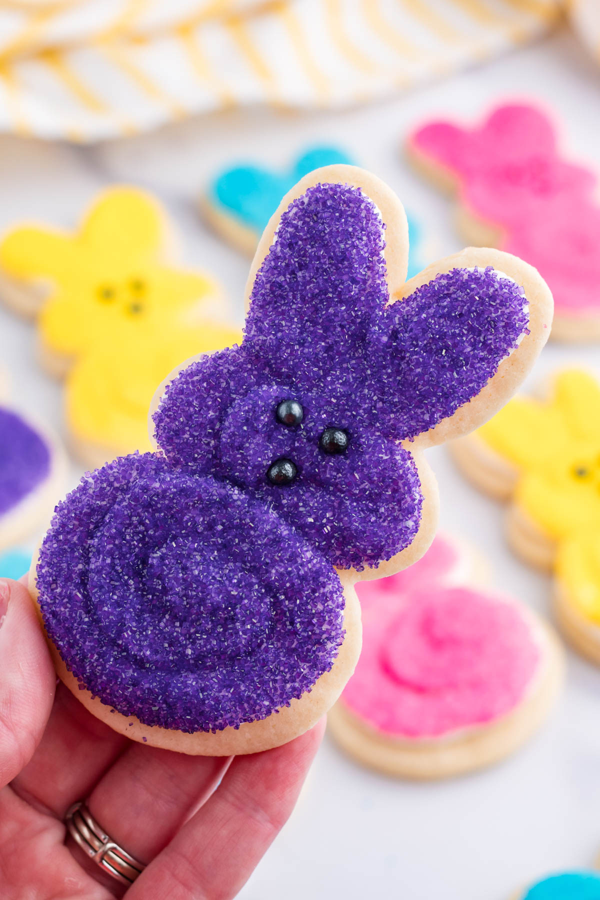 A hand holding up a purple Easter Bunny Cookie.