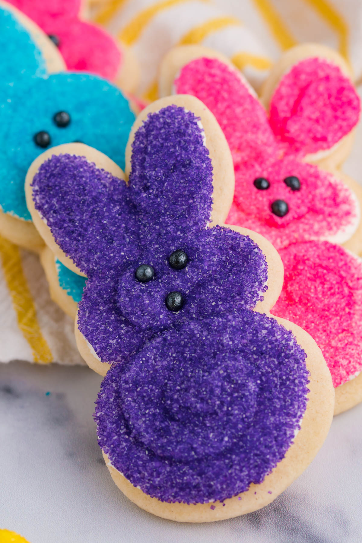A stack of multicolored Easter Bunny Cookies stacked on a white and yellow linen.