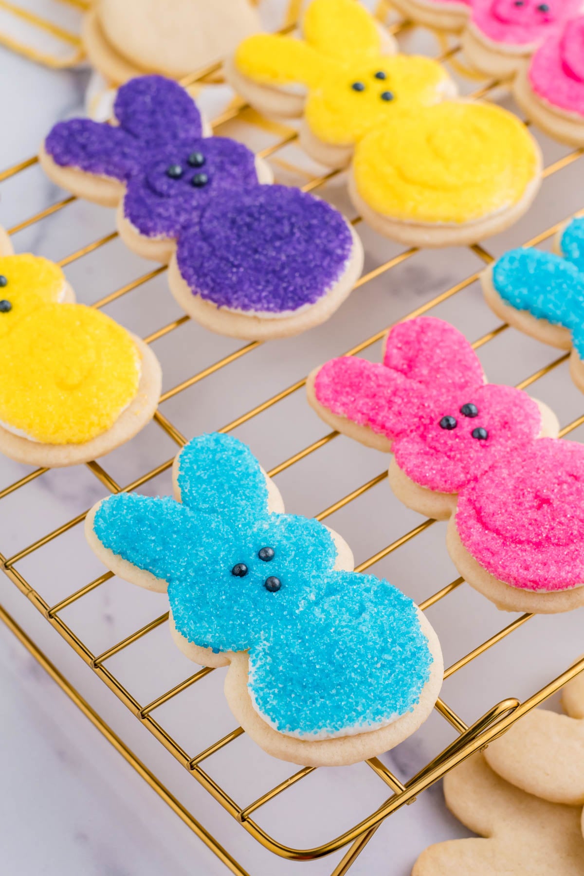Side view of multicolored Easter Bunny Cookies on a gold cooling rack.