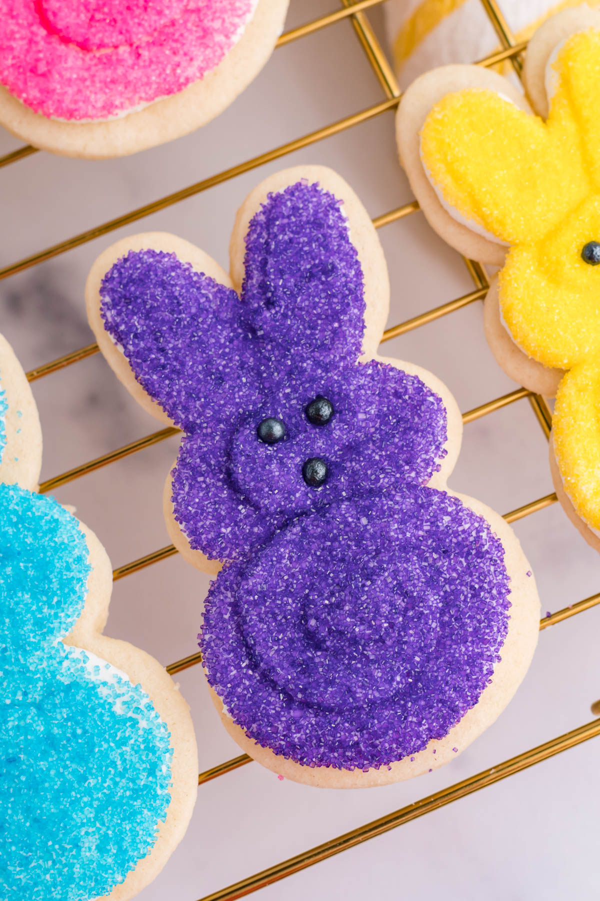 Overhead view of a purple bunny cookie on a gold cooling rack.