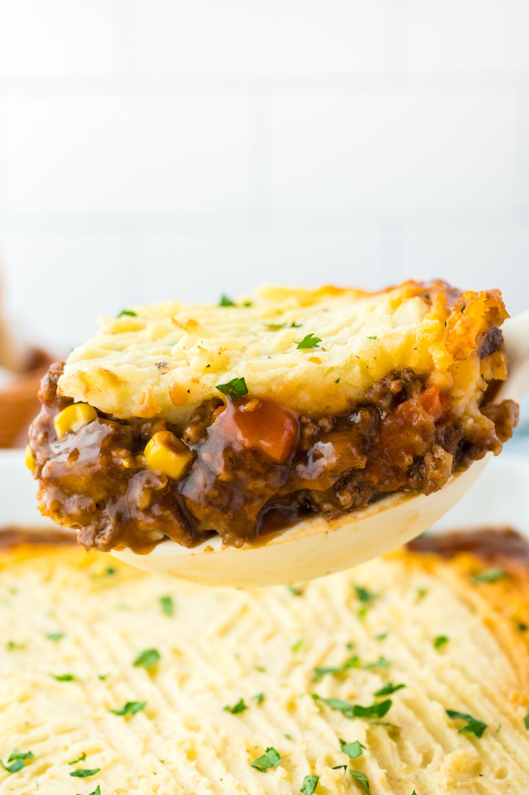 A large spoon removing Shepherd's Pie from the baking dish.