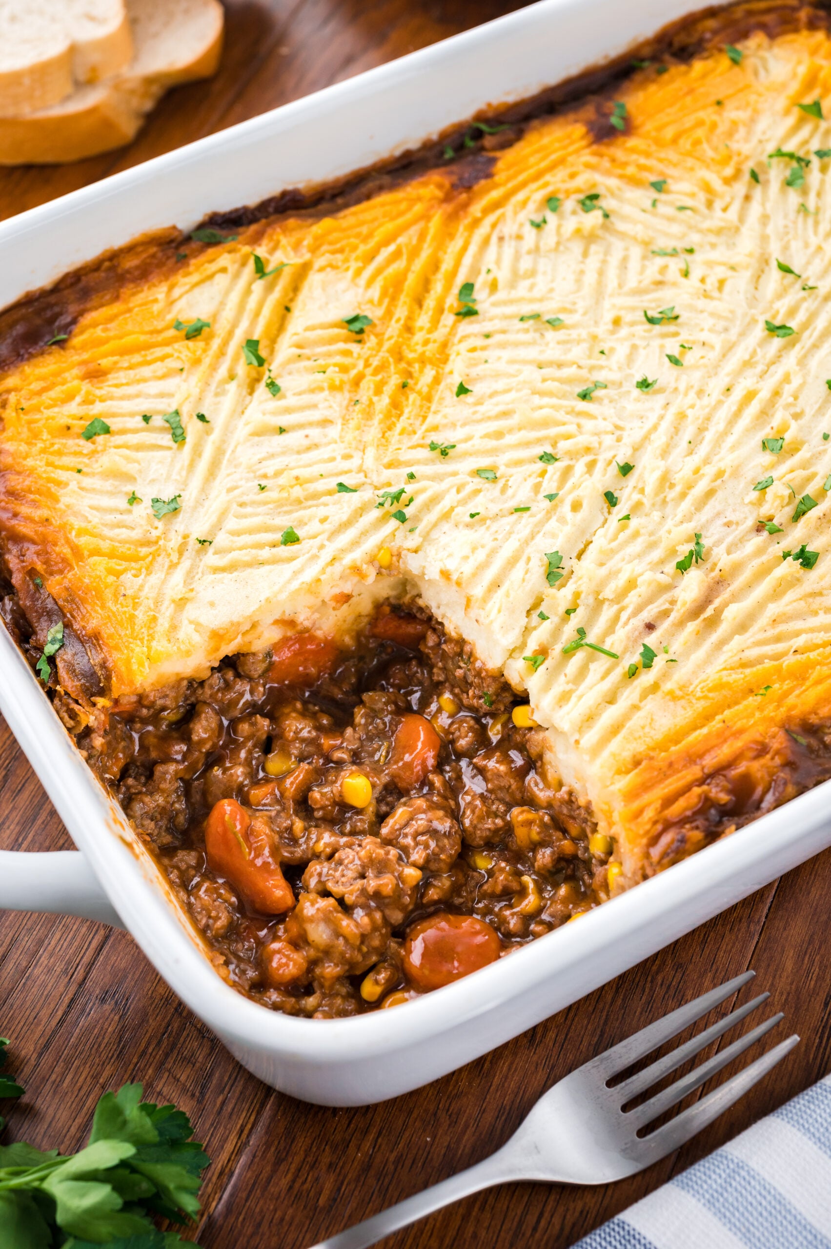A shot of the Shepherd's pie in a white baking dish with a piece removed showing the filling.