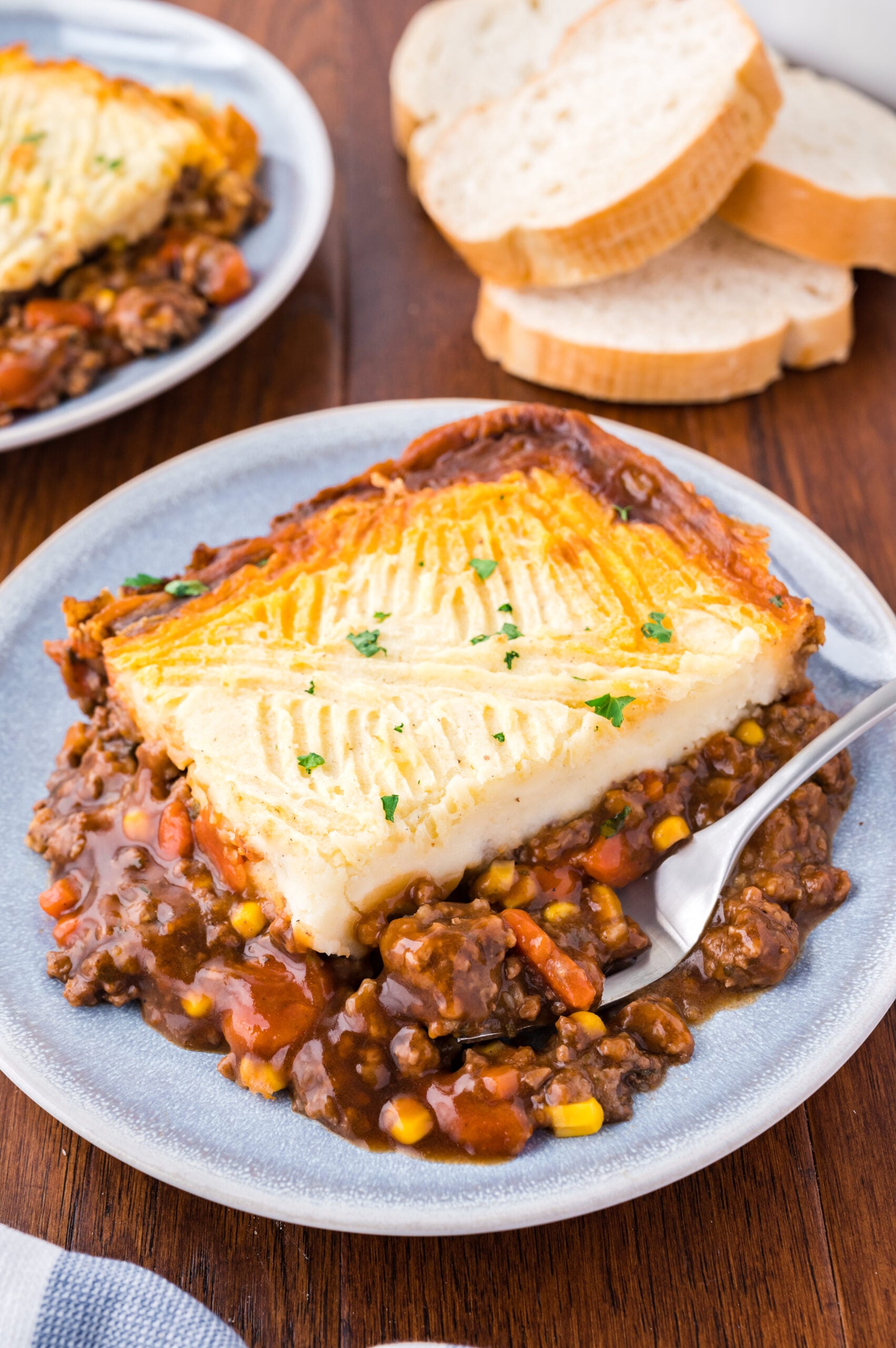 Shepherd's pie on a gray and white plate with a silver spoon.