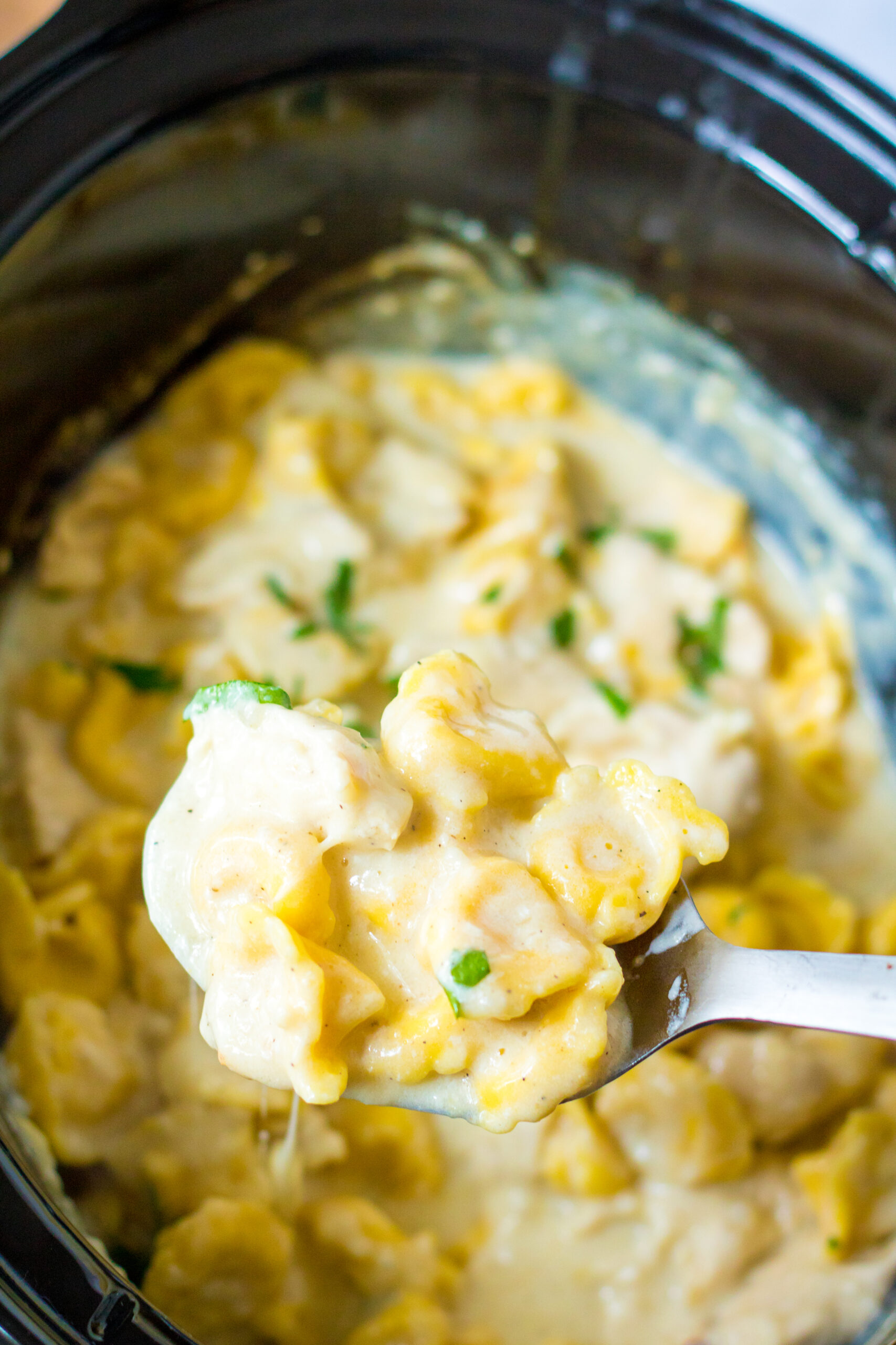 Overhead view of a bite of Slow Cooker Chicken Tortellini on a silver spoon.