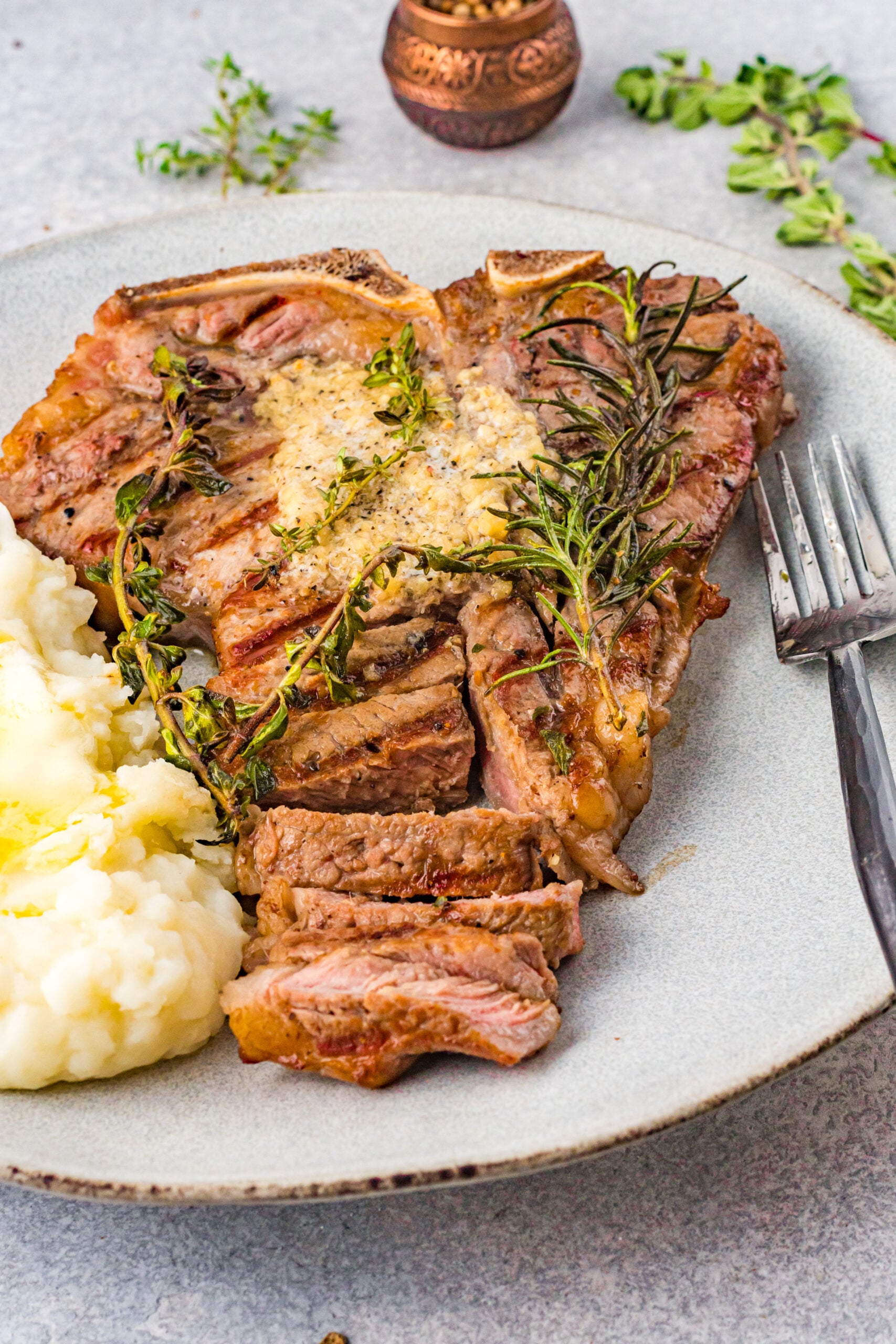 Front view of T Bone Steak on a white plate served with mashed potatoes.