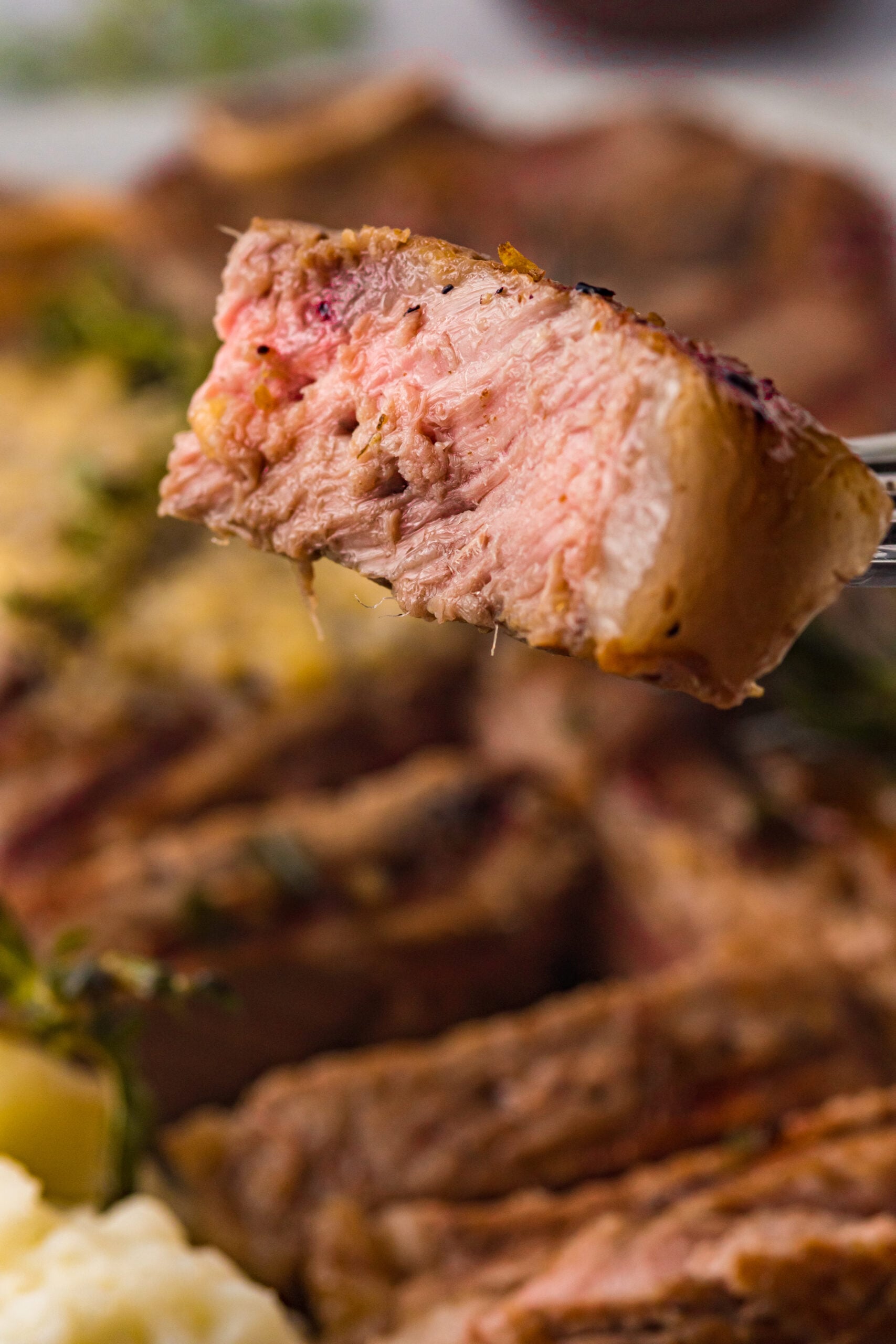 Close up view of a bite of T Bone Steak on a silver fork.