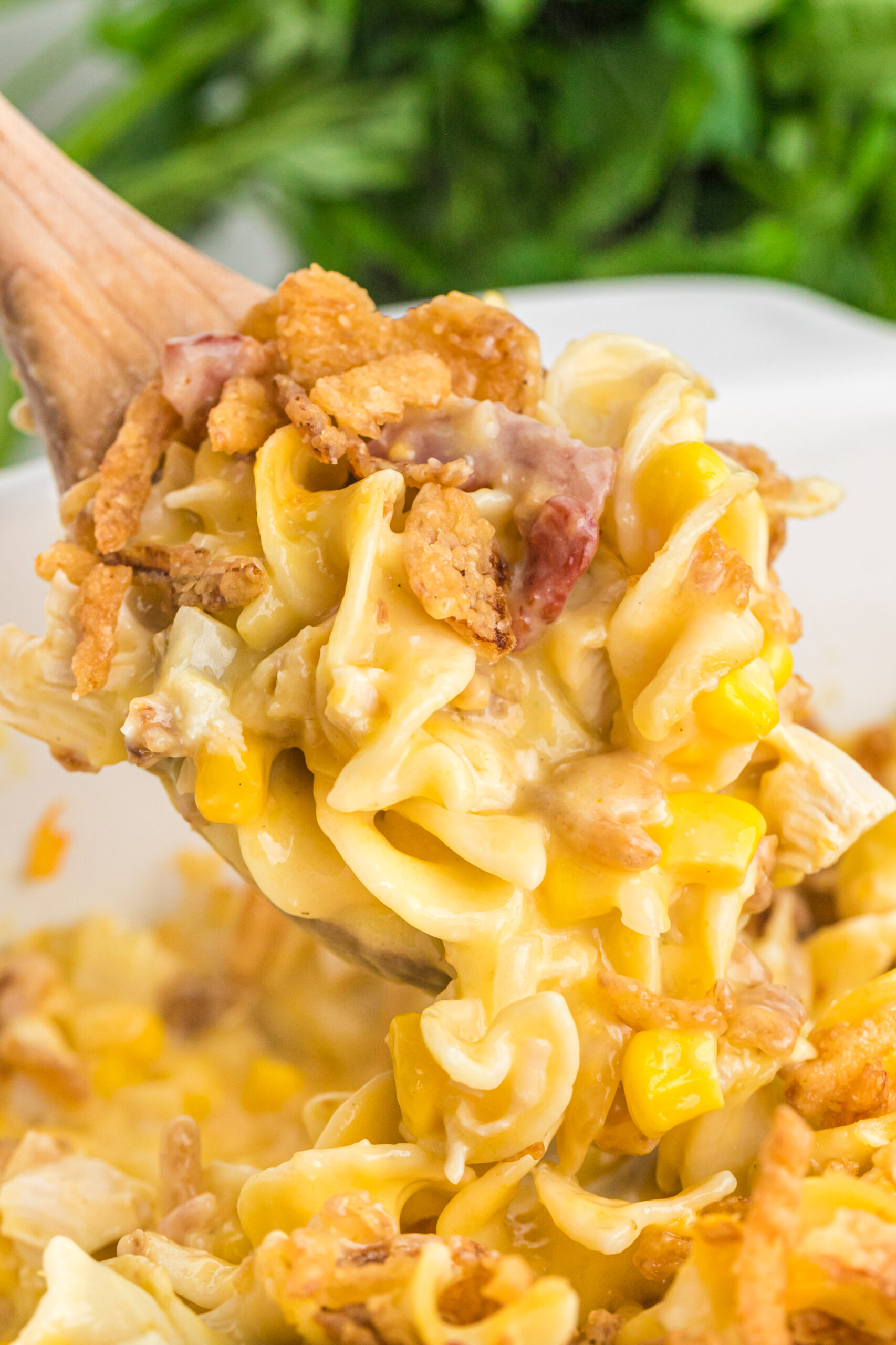 Close up view of Ultimate Chicken Casserole in a white baking dish with a scoop being lifted on a wooden spoon.
